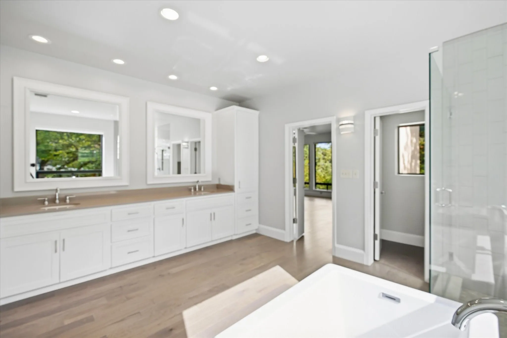 Dual vanity with integrated sinks, wood-finish flooring, recessed lighting, frameless glass shower, and a built-in soaking tub