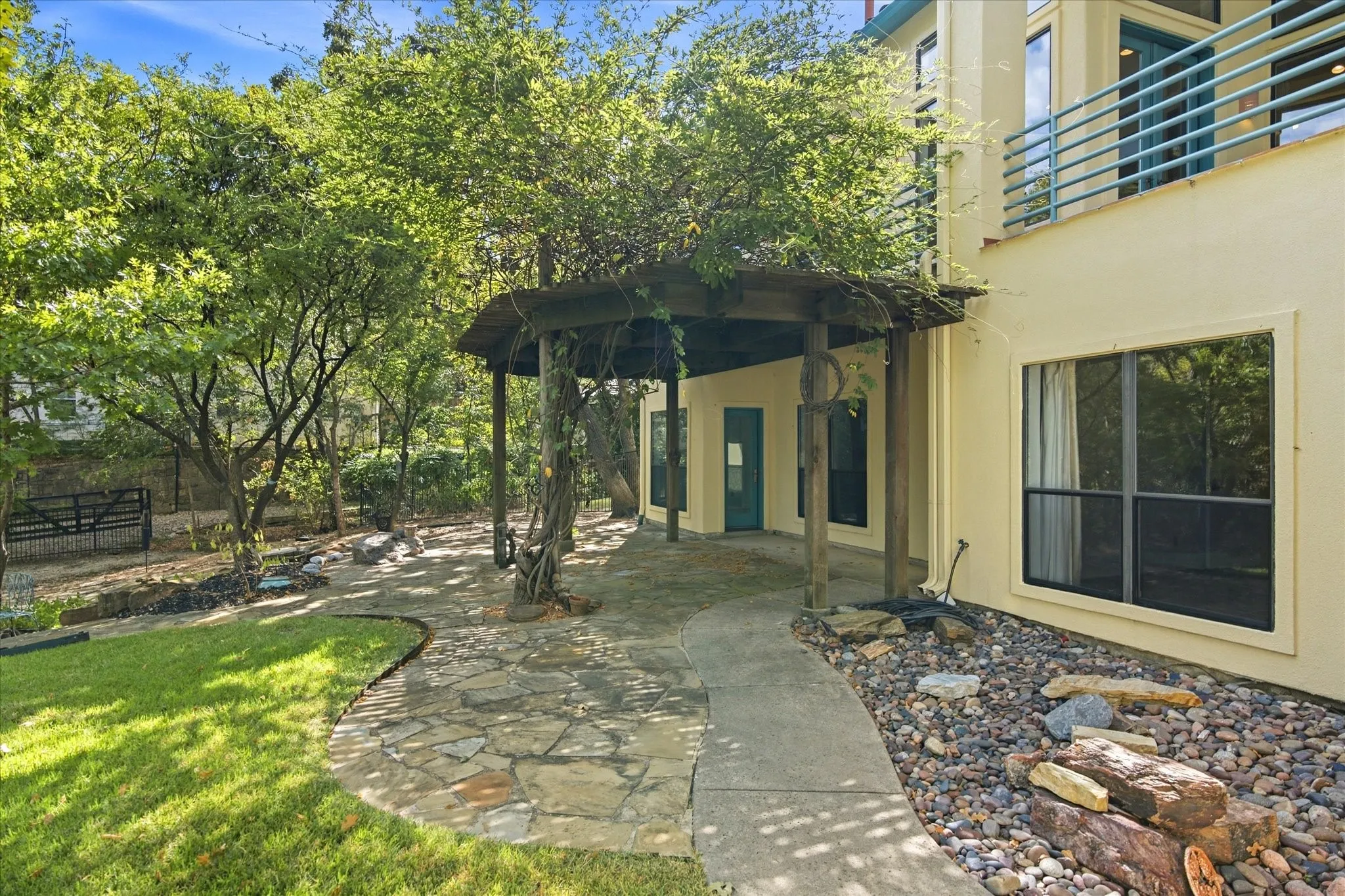 Exterior stucco finish with multiple windows, stone landscaping, and a covered pathway leading to an additional entrance
