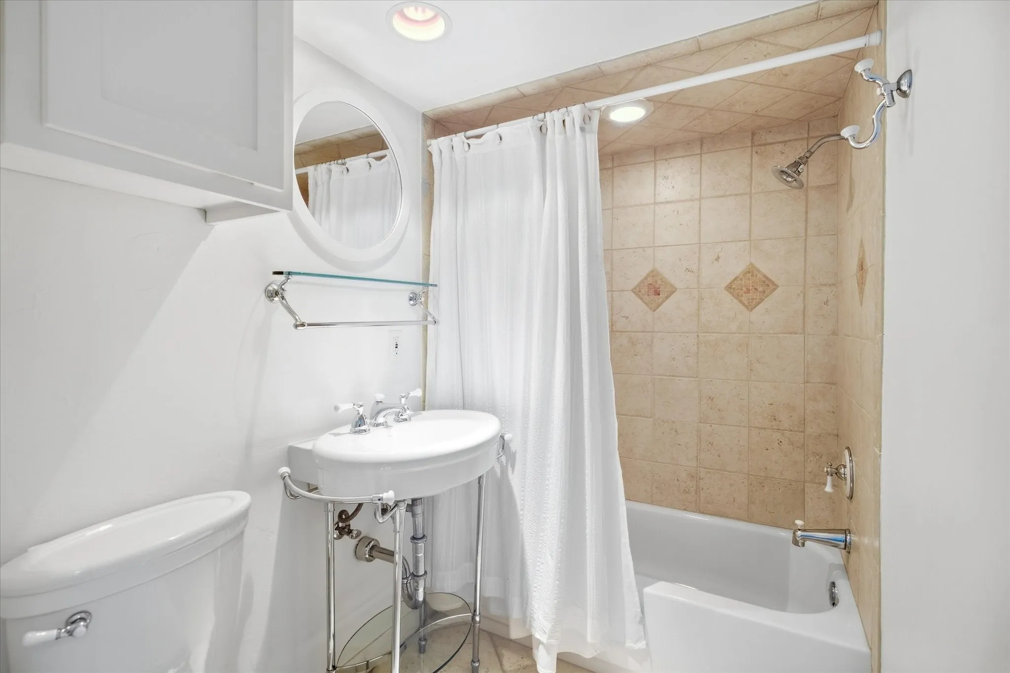 Pedestal sink with chrome fixtures, tiled shower surround, built-in shelving, white cabinetry, and recessed lighting