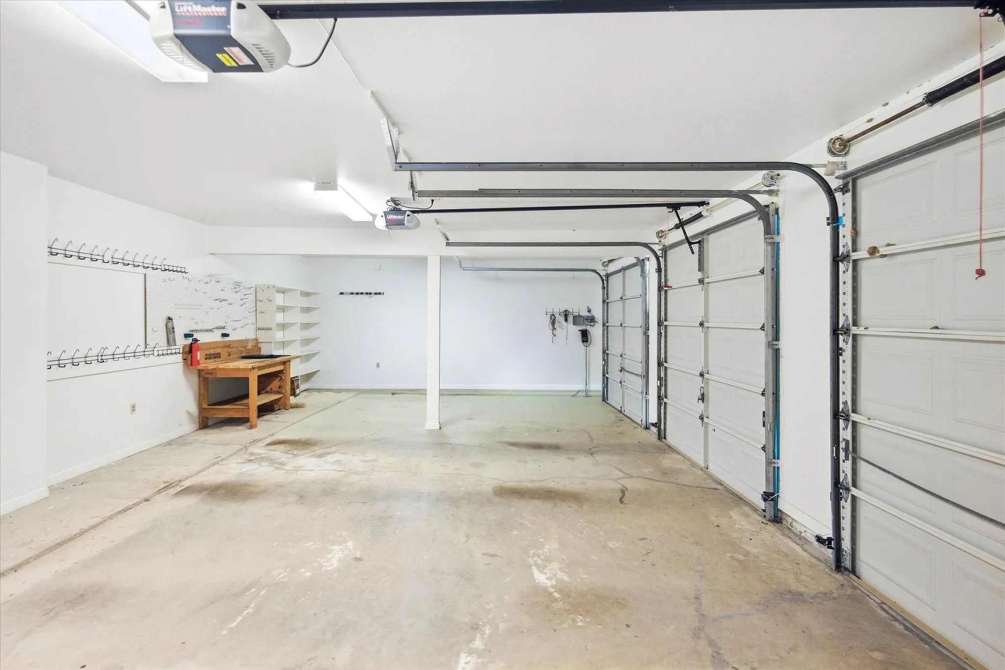 Three garage doors, concrete flooring, overhead lighting, and built-in shelving