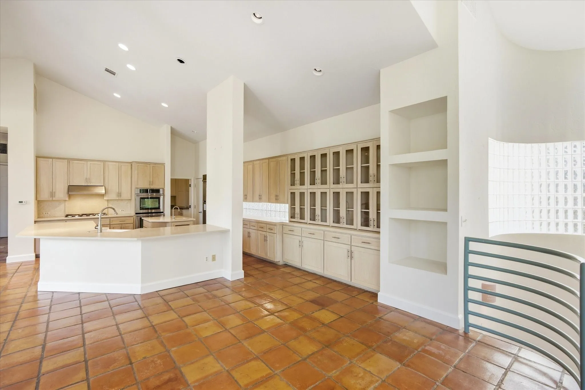 Expansive kitchen featuring wood cabinetry, integrated stainless steel appliances, a large island with sink, and terracotta tile flooring