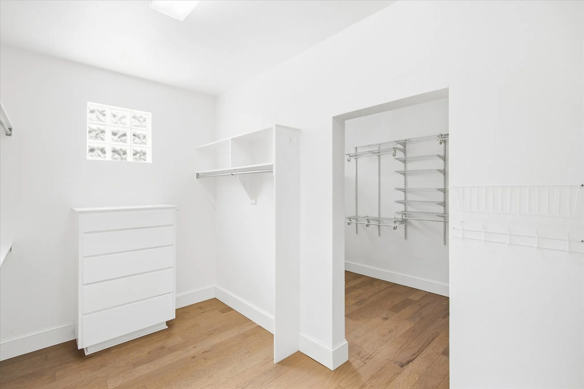 Wood-finish flooring throughout, featuring a built-in five-drawer chest, glass block window, and integrated shelving with hanging rods