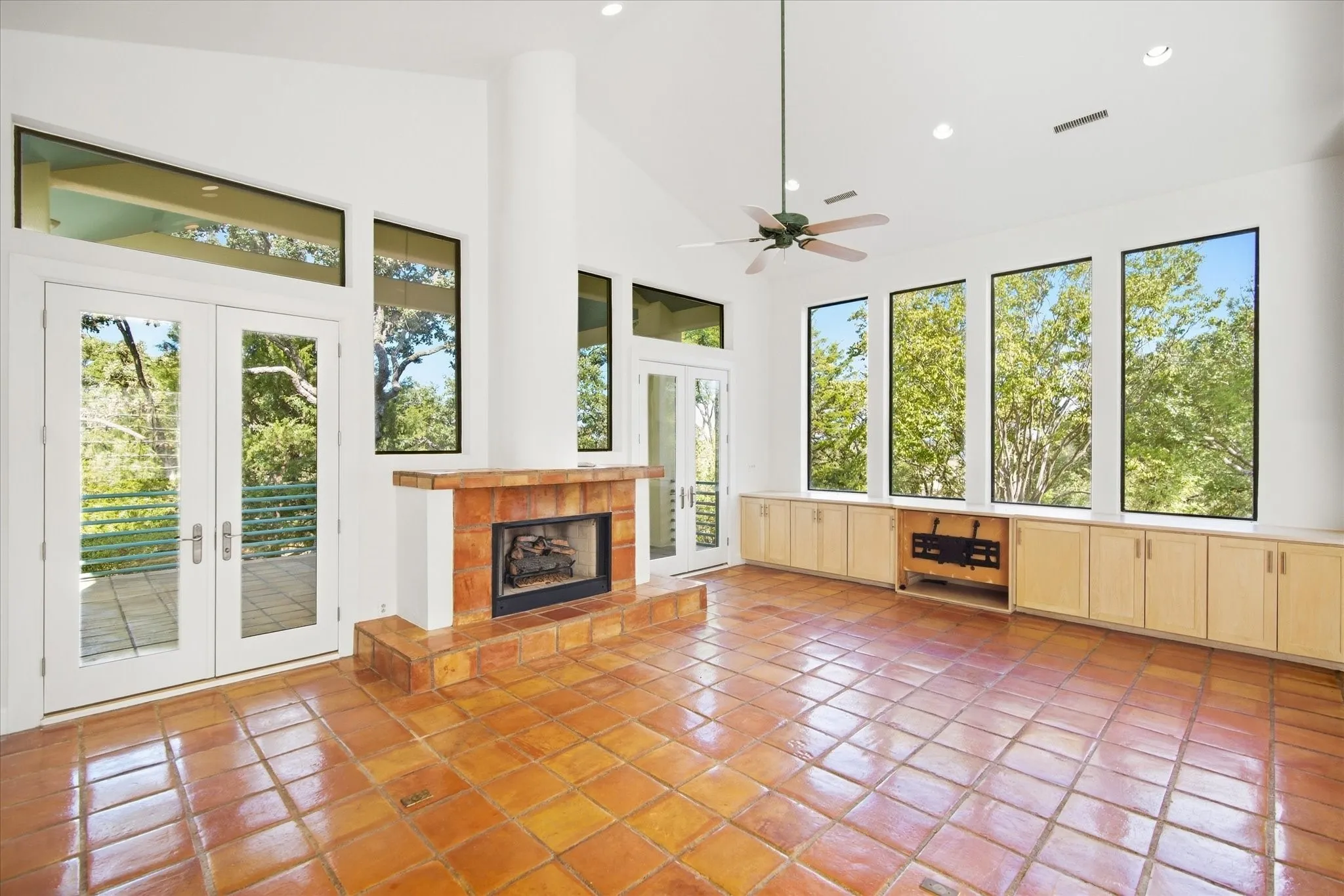 Vaulted ceiling, ceiling fan, fireplace with tile surround, built-in cabinetry, and tile flooring