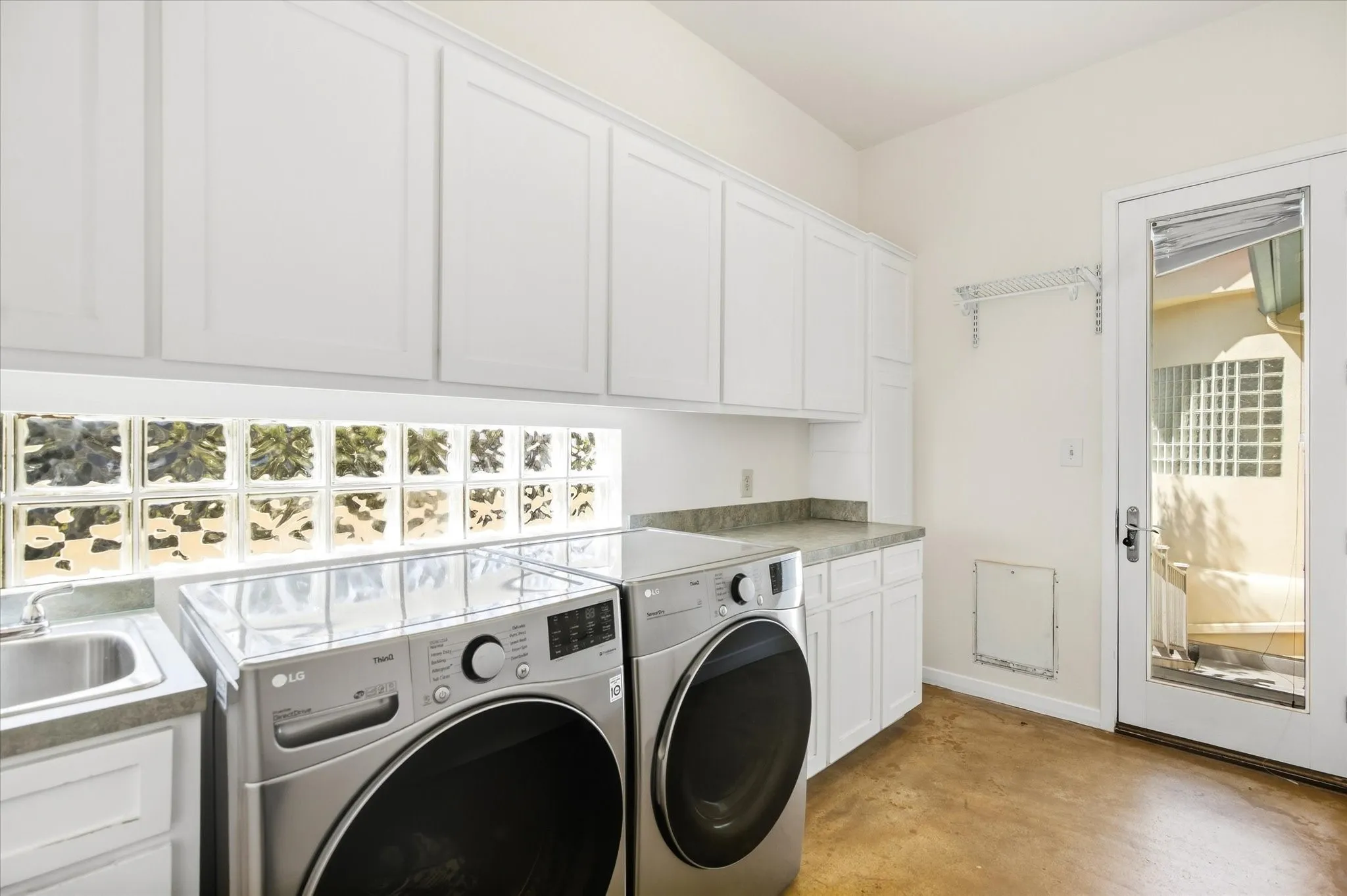 White upper and lower cabinetry, glass block window, utility sink, counter space, and a glass-paneled door