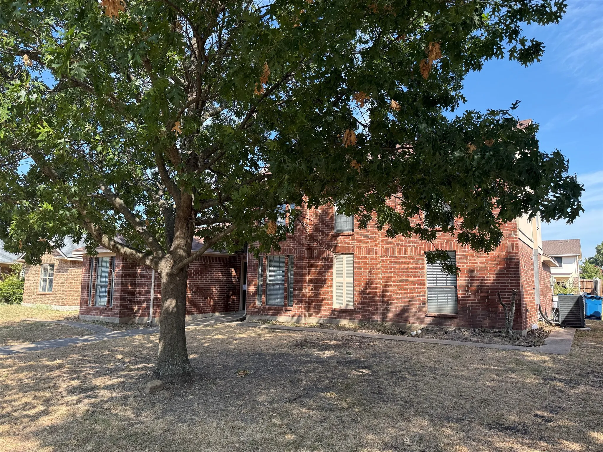 Red brick exterior with multiple windows and a mature front yard tree