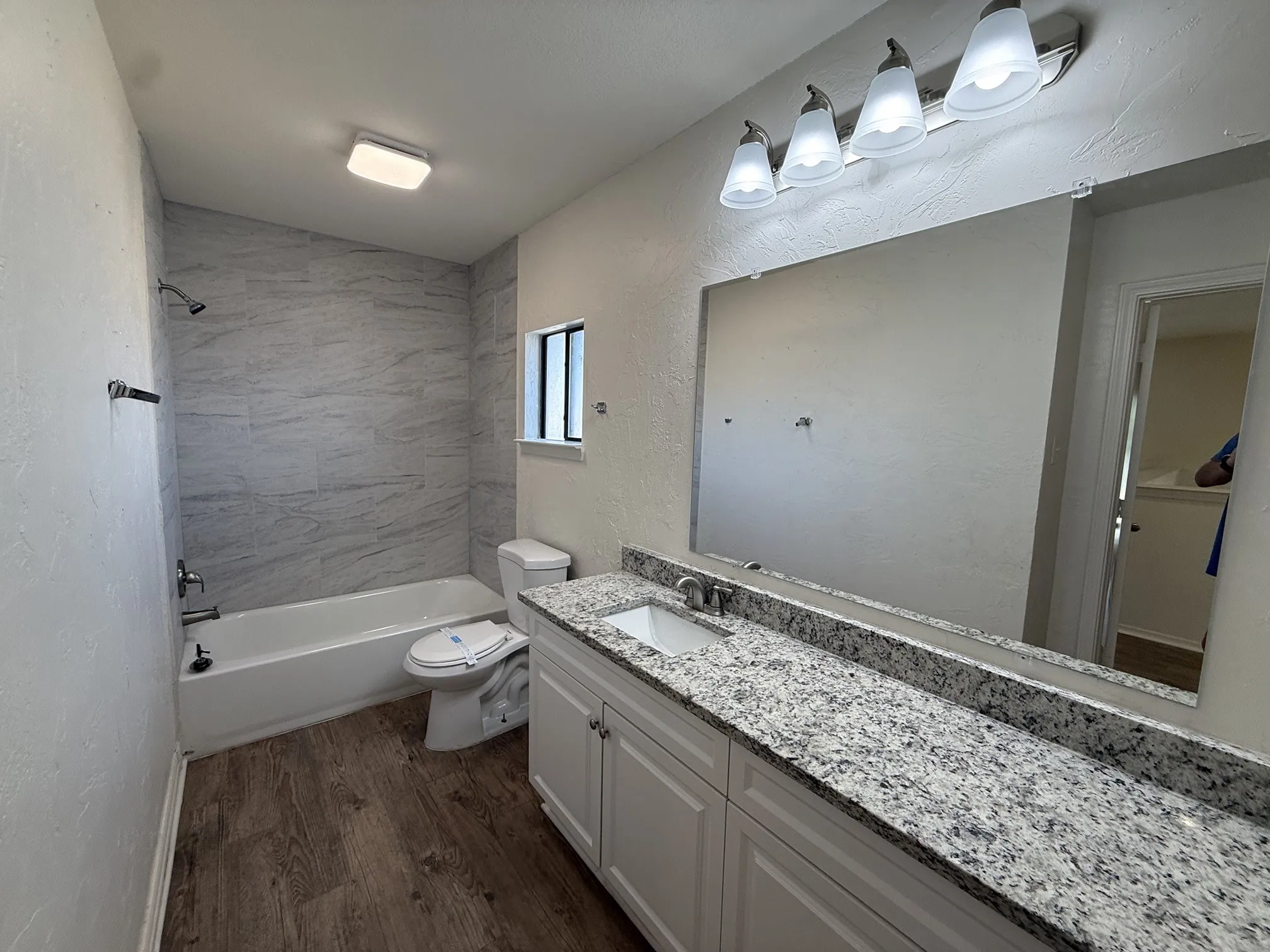 Spacious bathroom featuring a white vanity with a light-toned countertop, wood-finish flooring, a white bathtub, and tiled shower surround