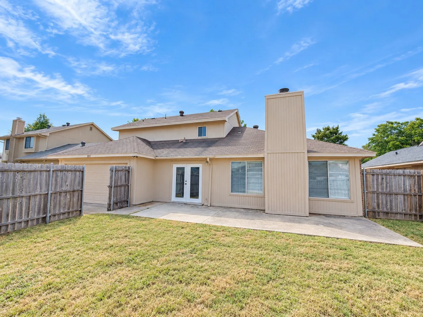 Expansive backyard with a concrete patio, wood fencing, and a two-story exterior
