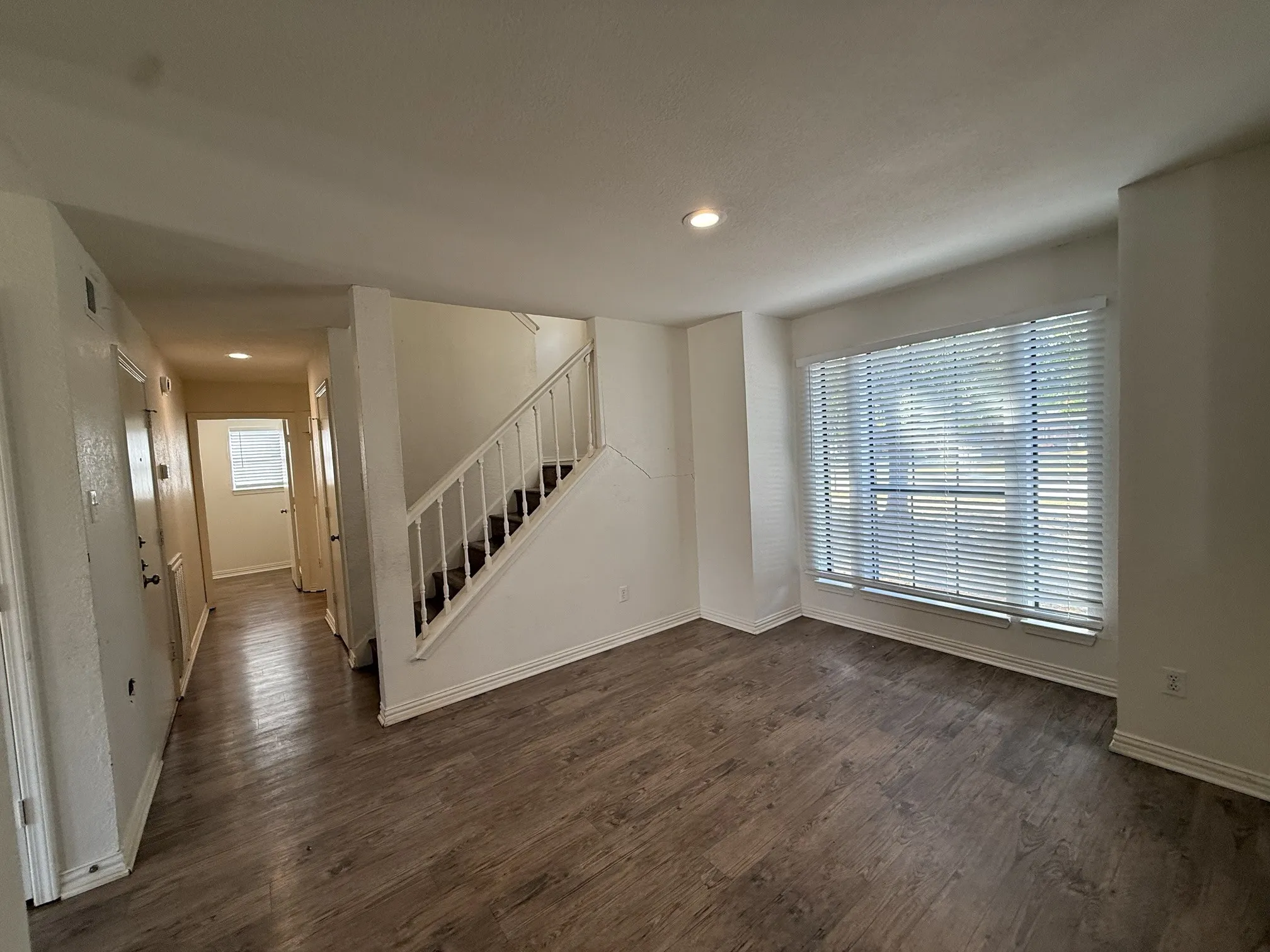 Wood-finish flooring, recessed lighting, staircase with white railing, and a window with blinds