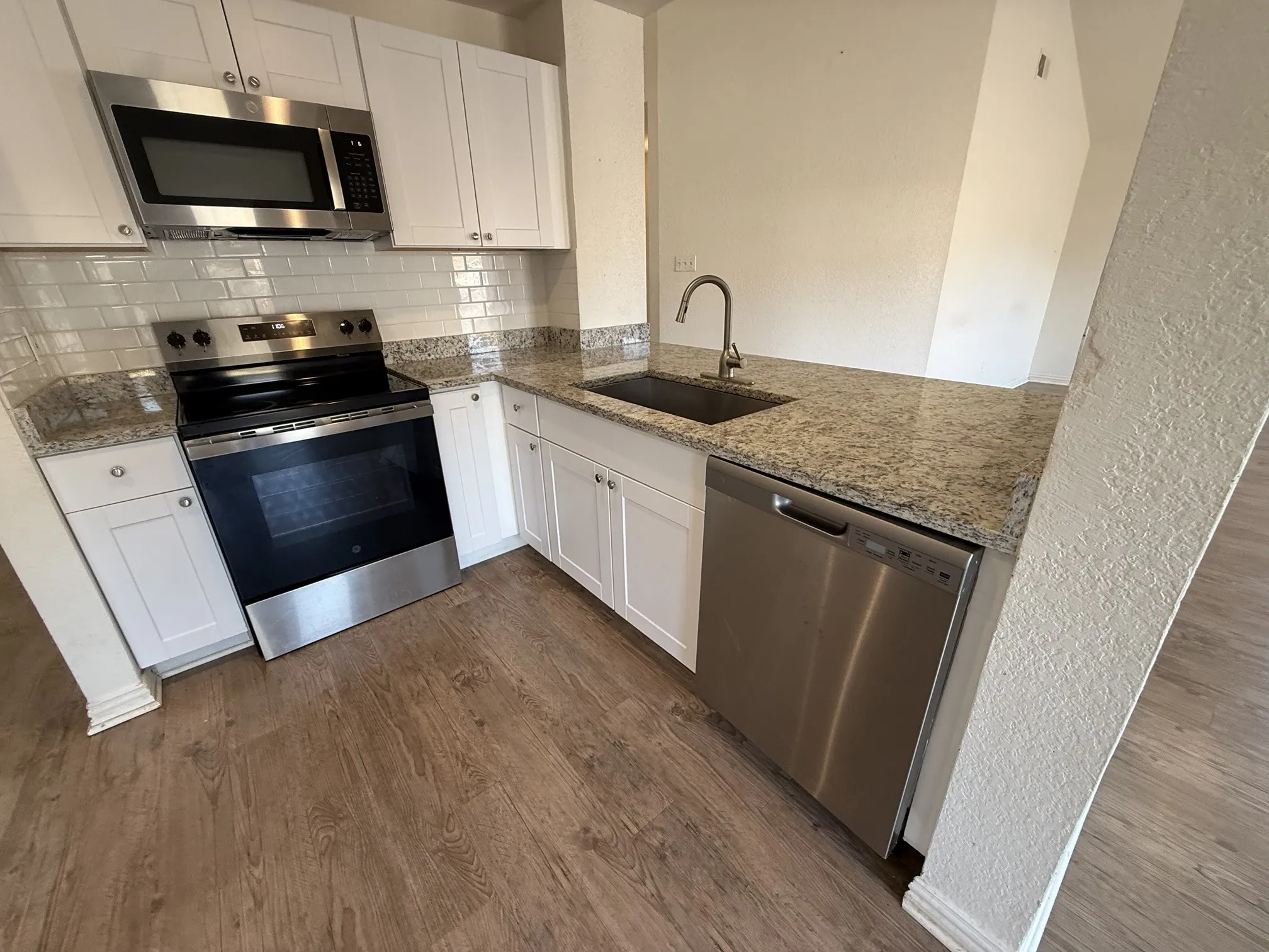 Kitchen featuring white cabinetry, granite countertops, a stainless steel appliance suite, subway tile backsplash, and wood-finish flooring
