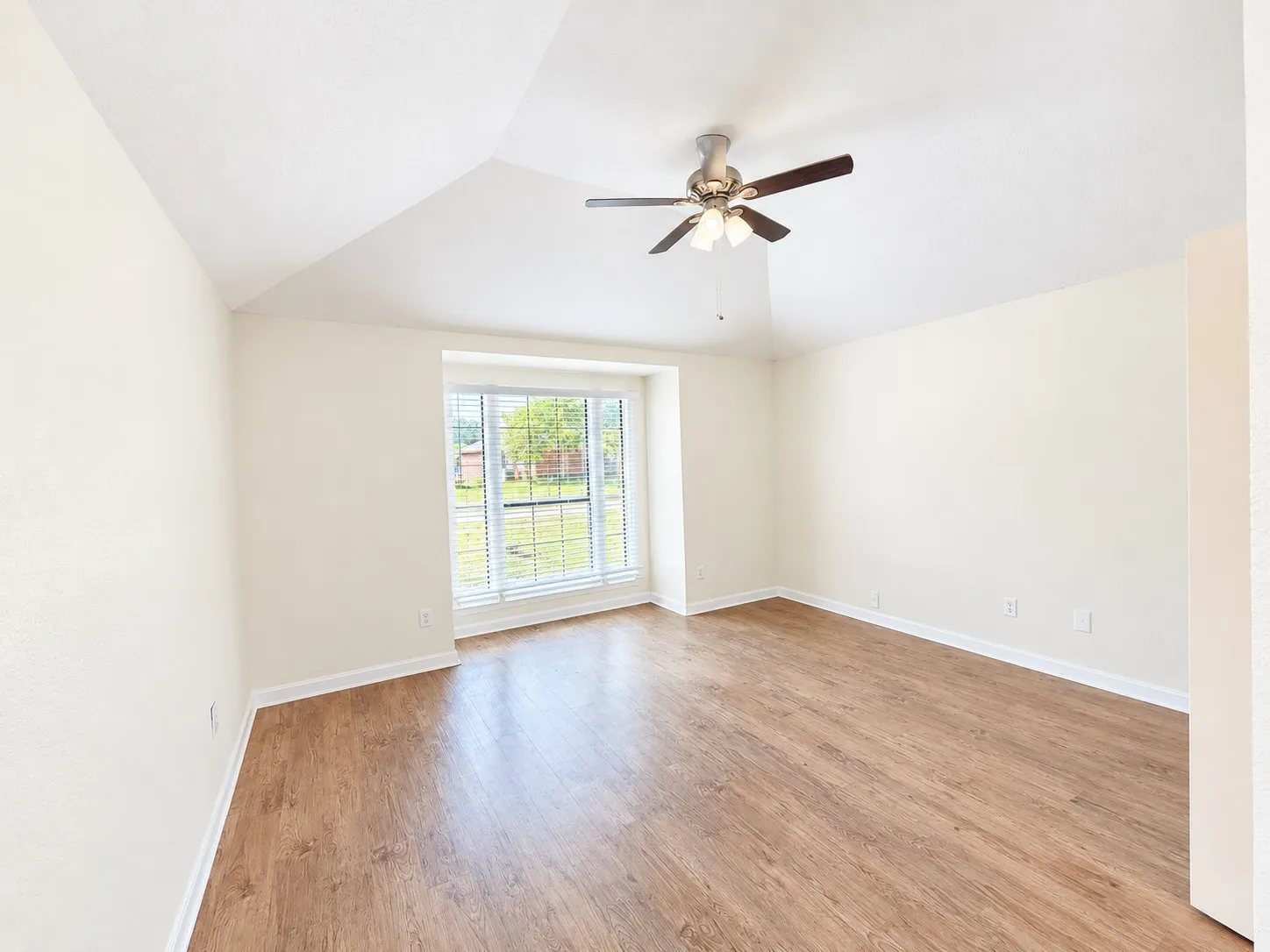 Vaulted ceiling, wood-finish flooring, ceiling fan with light fixture, and a bay window