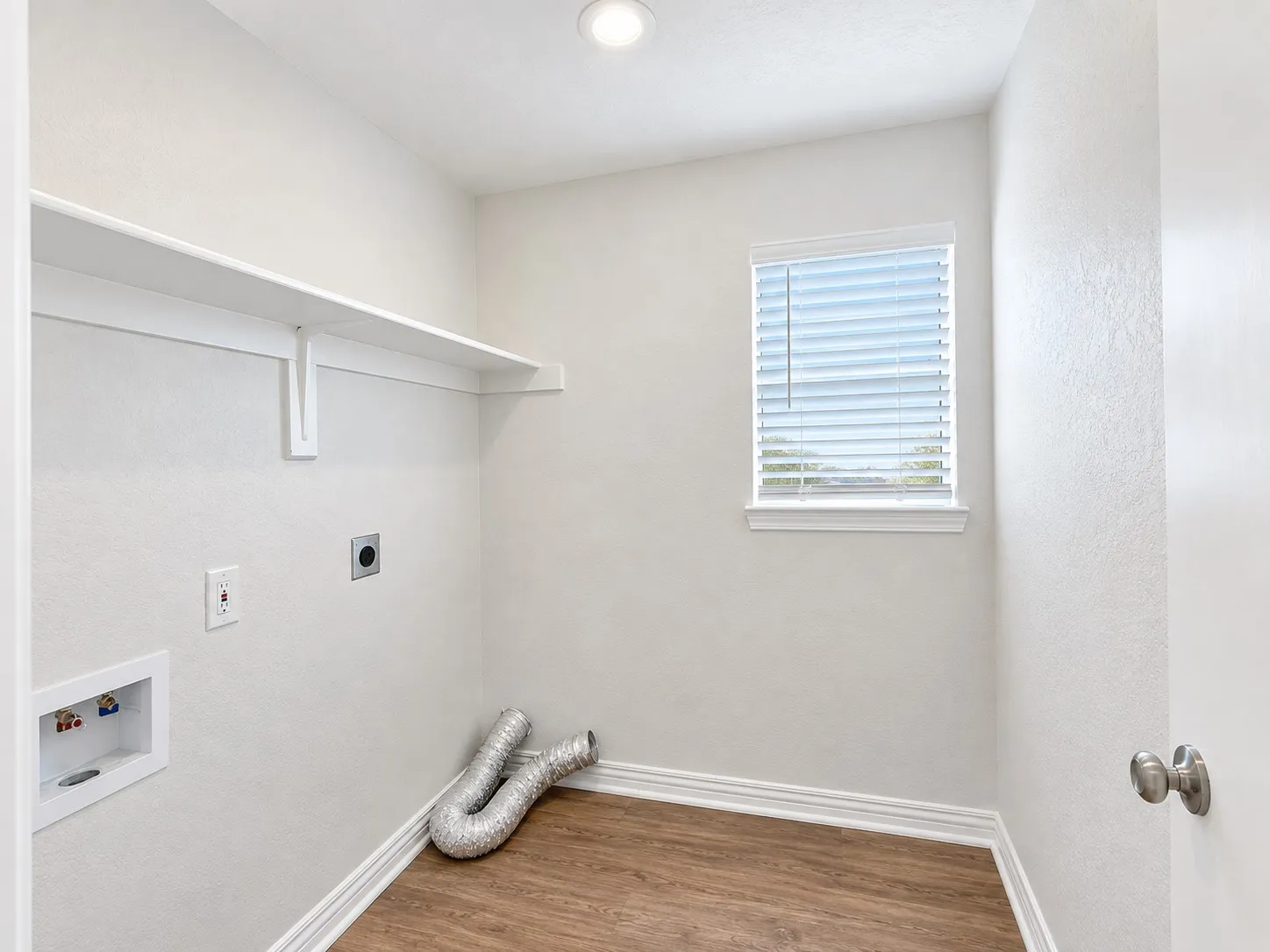 Laundry area featuring wood-finish flooring, a built-in shelf, and a window with blinds