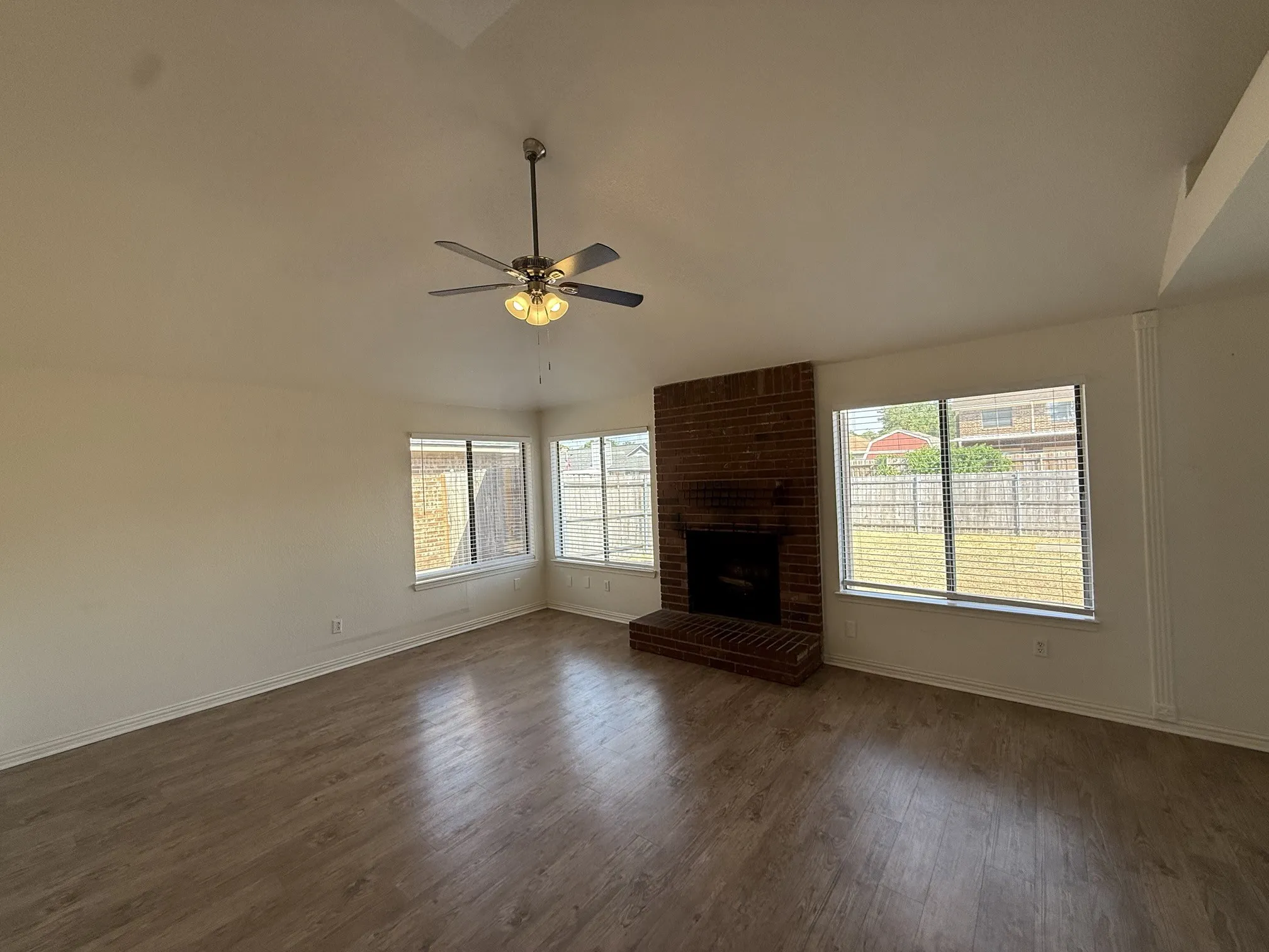 Vaulted ceiling with a ceiling fan, brick fireplace, wood-finish flooring, and multiple windows