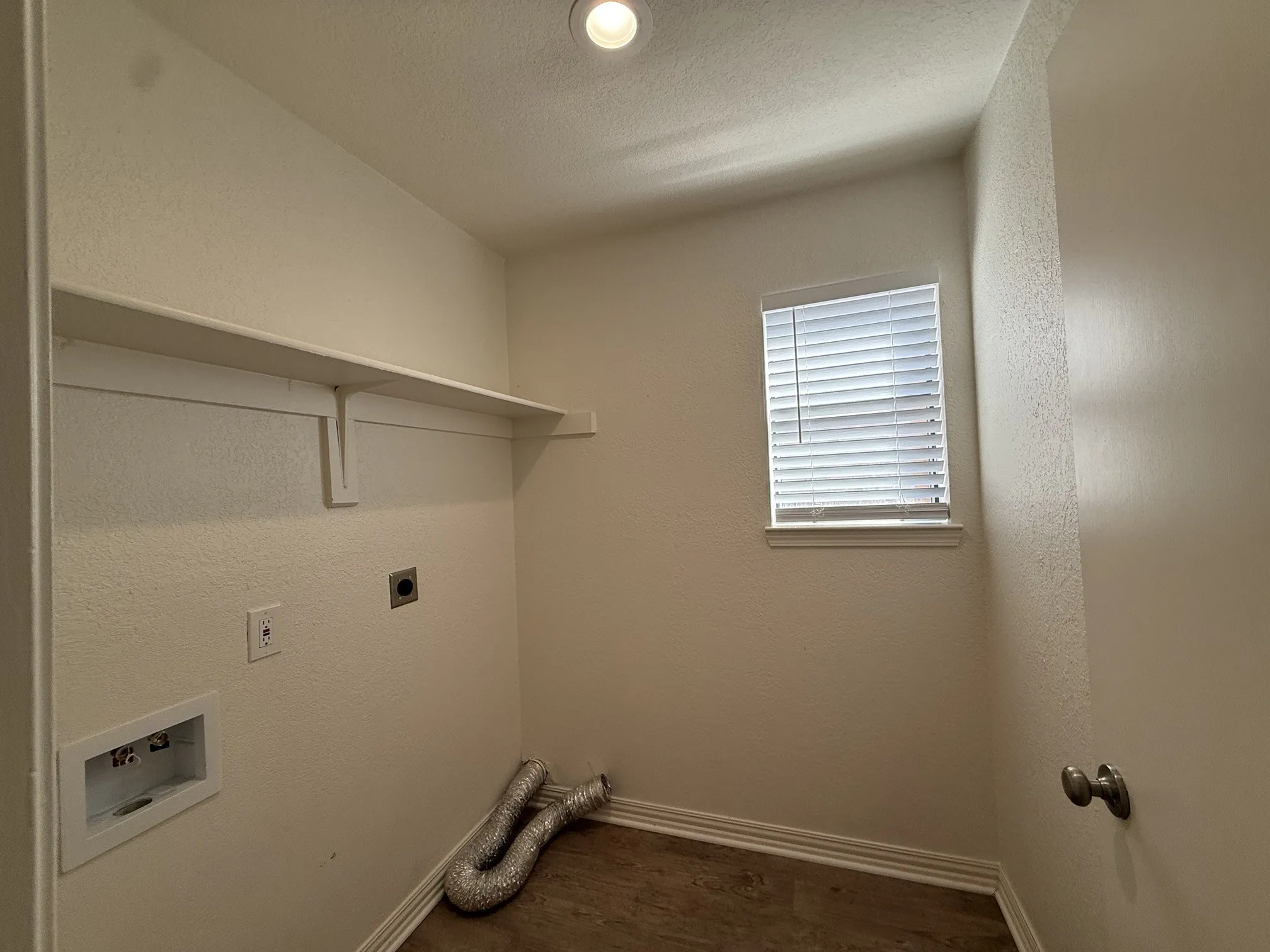 Dedicated laundry area featuring a window with blinds, wood-finish flooring, and a built-in wall shelf