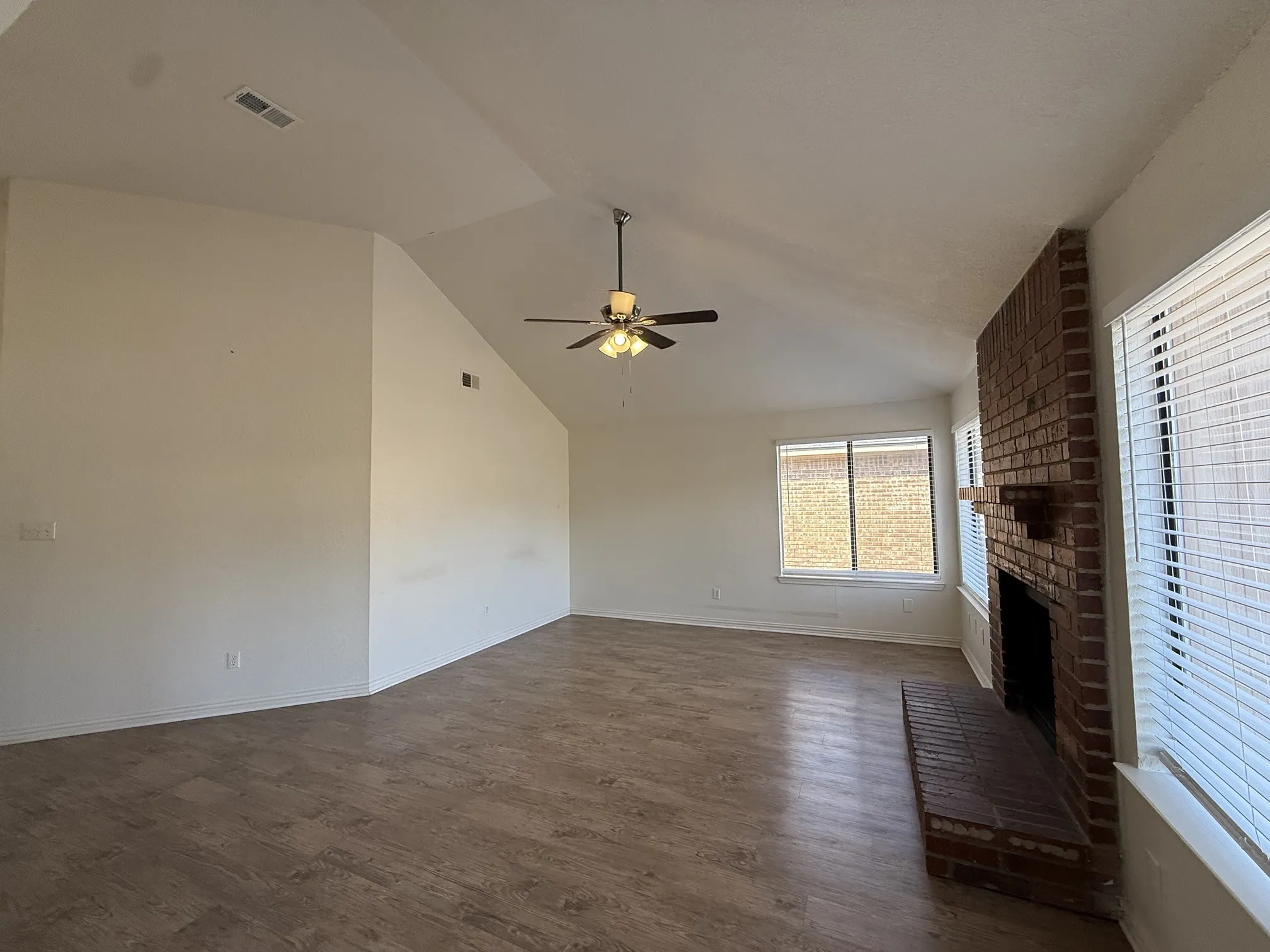 Vaulted ceiling with a ceiling fan, brick fireplace, and wood-finish flooring