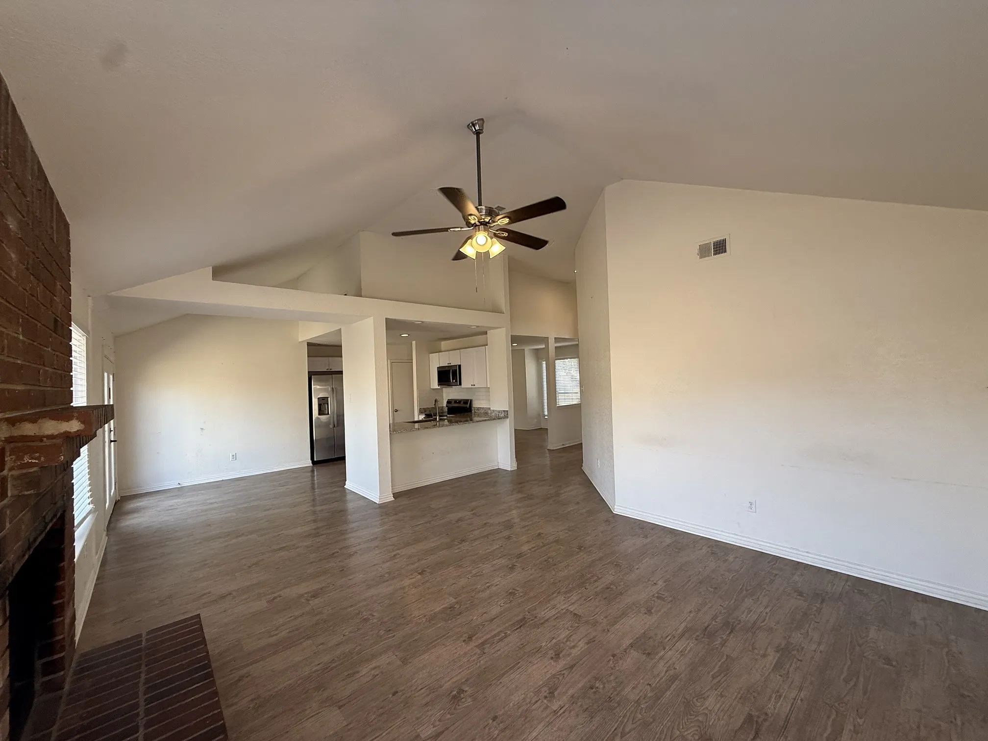 Vaulted ceilings with a ceiling fan, brick fireplace, wood-finish flooring, and white cabinetry