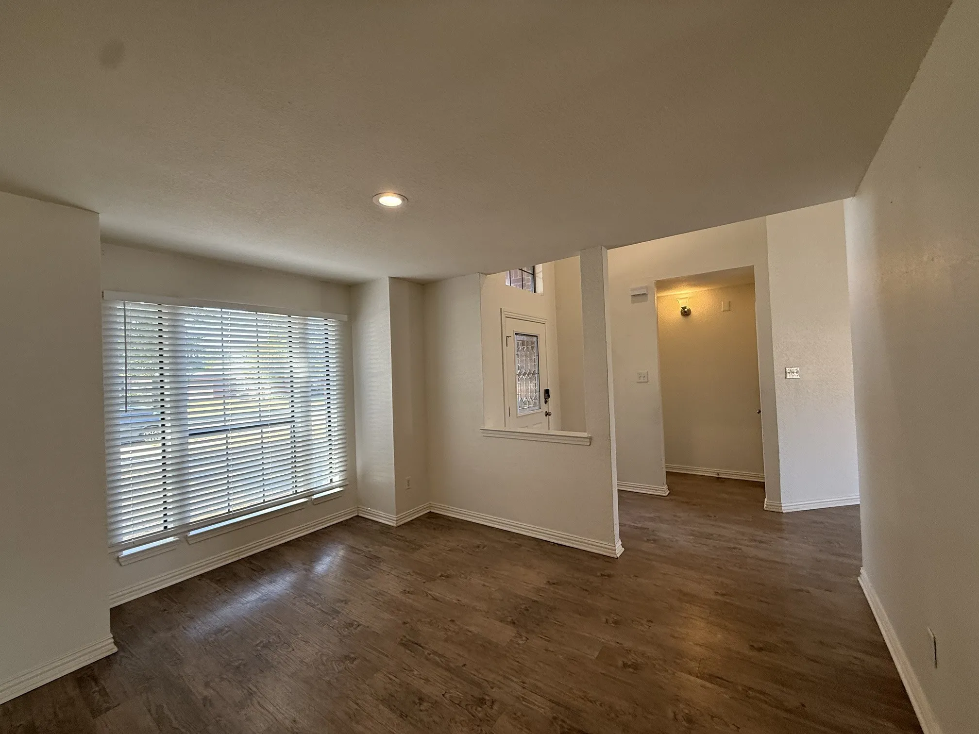 Wood-finish flooring throughout, recessed ceiling lighting, a large window with blinds, and white painted walls