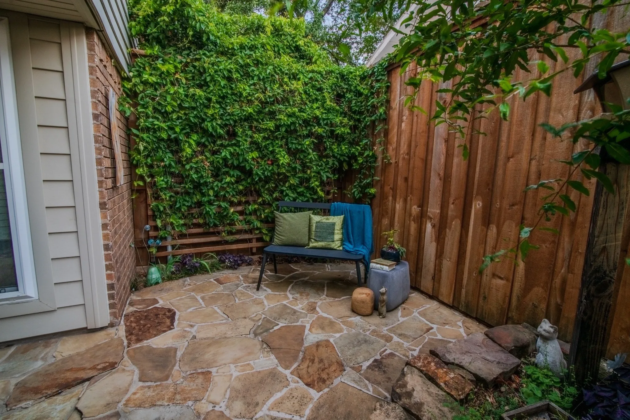 Flagstone patio with a natural wood privacy fence, brick exterior, and lush green climbing plants