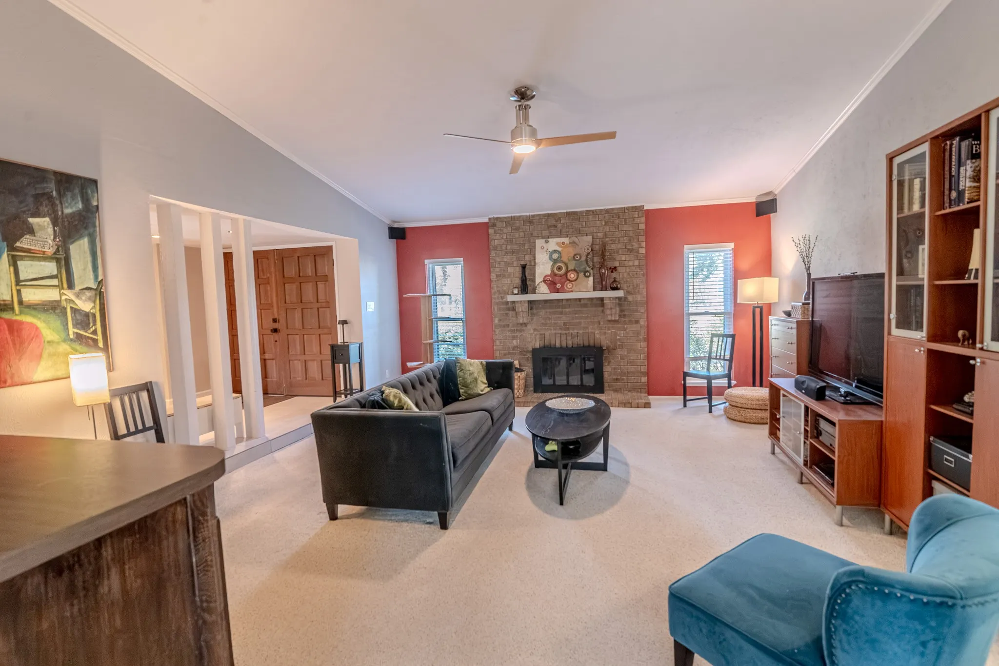 Vaulted ceiling with a ceiling fan, brick fireplace, built-in shelving, wood-finish flooring, and a paneled entry door