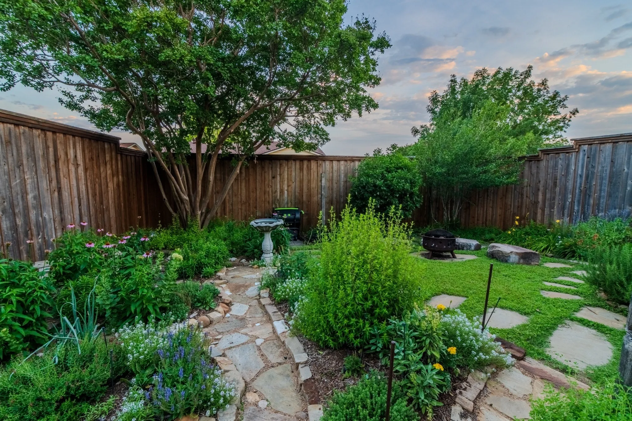 Private fenced backyard featuring a stone pathway, established landscaping, and a central lawn area