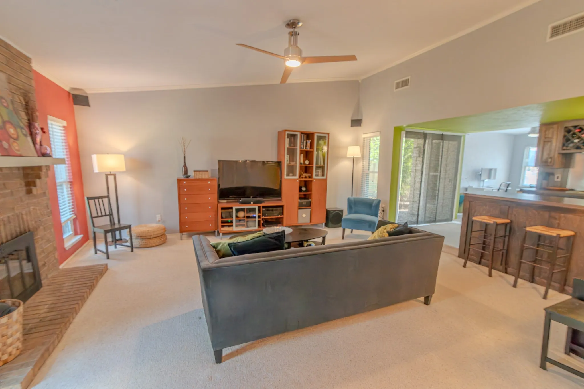 Vaulted ceiling with ceiling fan, brick fireplace, built-in bar with seating, recessed lighting, and large windows with blinds