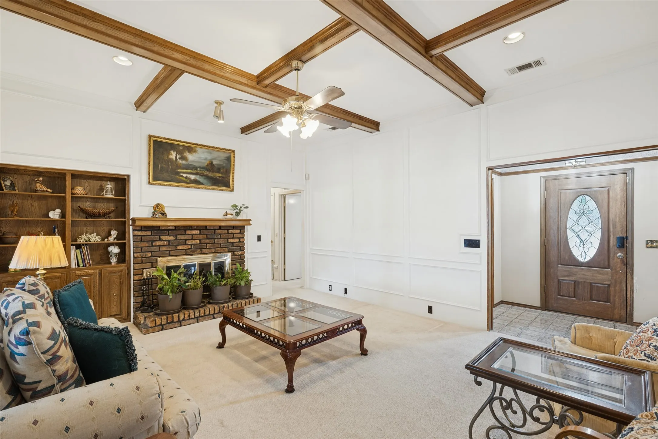 Exposed wood ceiling beams, brick fireplace, built-in shelving, decorative wall paneling, and a wood-paneled door with an oval glass insert. Freshly painted. Designer carpet.