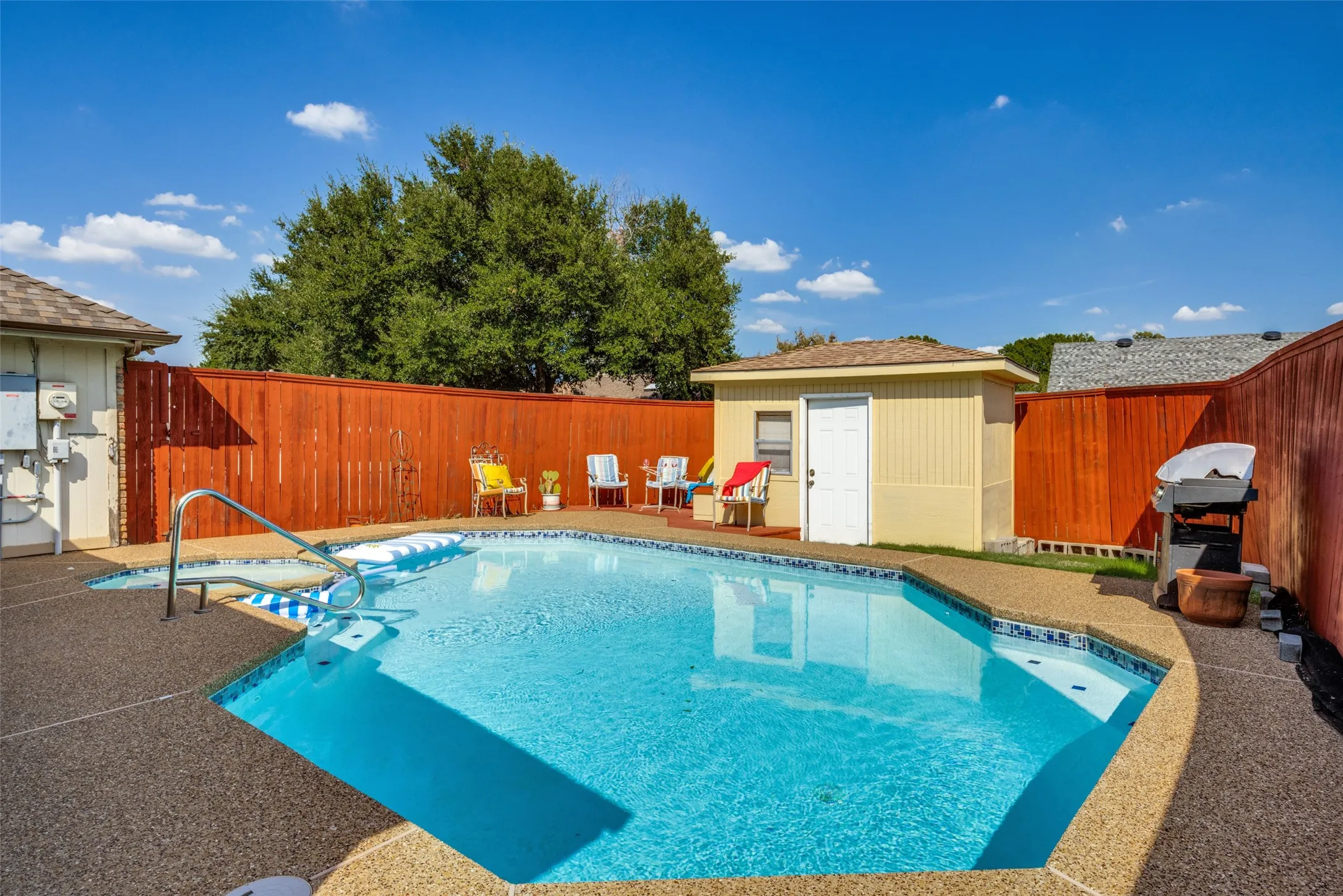 Outdoor pool and spa with textured concrete decking, metal pool handrails, and a dedicated storage shed featuring electricity.