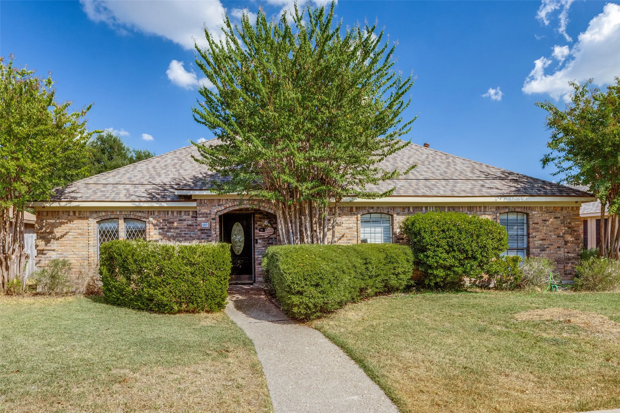 Brick exterior with an arched entryway, decorative front door, and mature landscaping