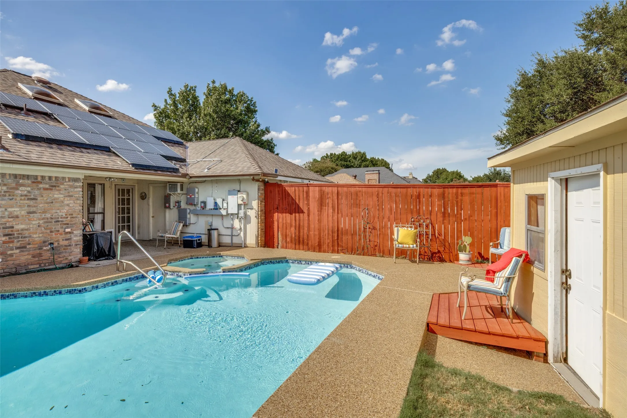 Swimming pool with integrated spa, surrounding concrete decking, private wood fencing, and solar panel array