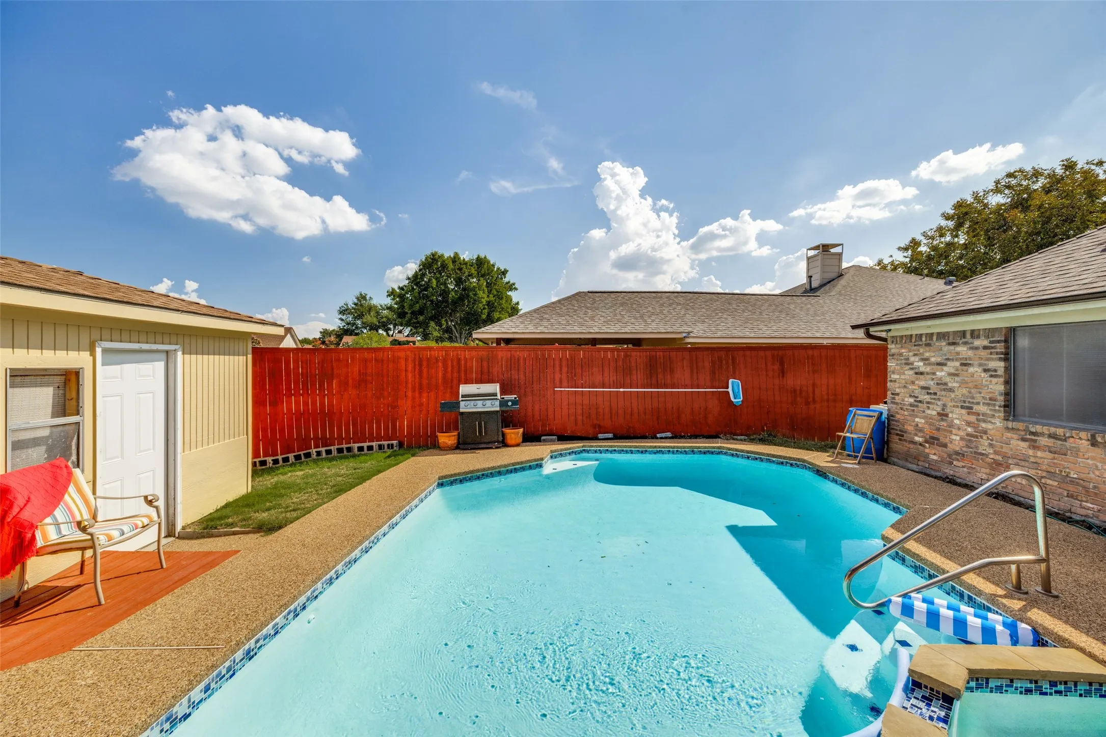 In-ground swimming pool with an integrated spa, complemented by a surrounding concrete deck and a privacy fence