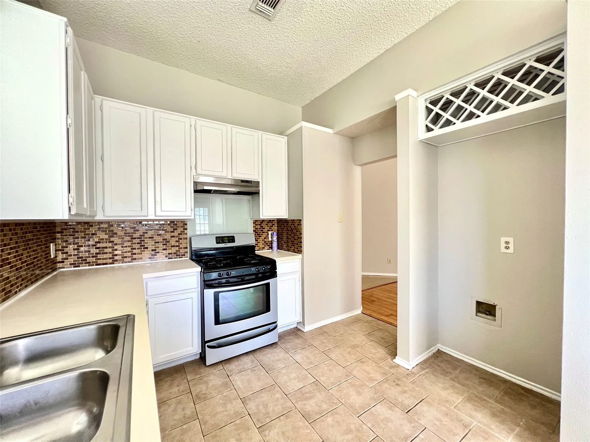 Kitchen with light countertops, tasteful backsplash, gas stove, and under cabinet range hood