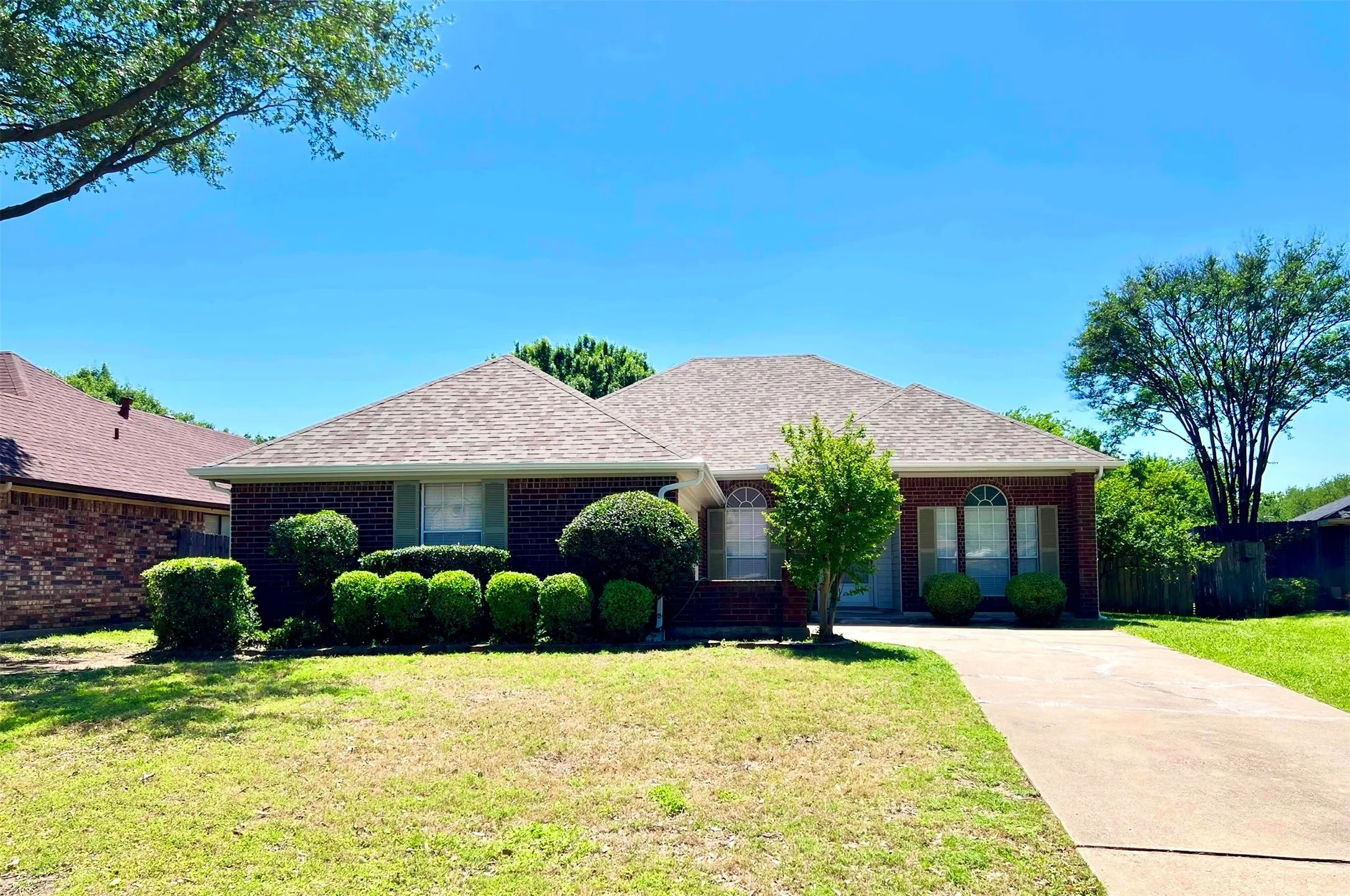 Ranch-style home featuring fence, roof with shingles, concrete driveway, brick siding, and a front yard