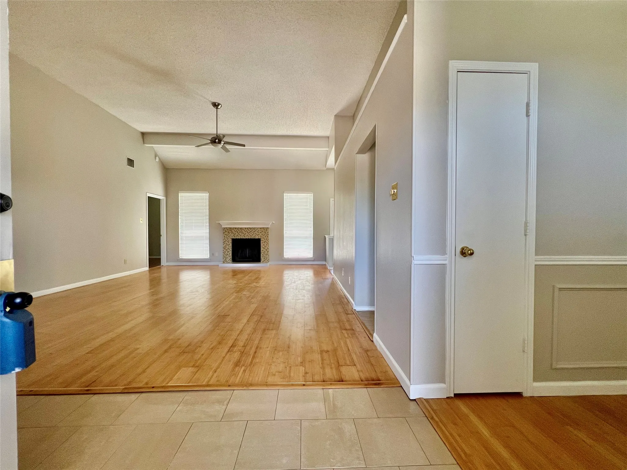 Unfurnished living room featuring ceiling fan, baseboards, a fireplace with raised hearth, and light wood-type flooring