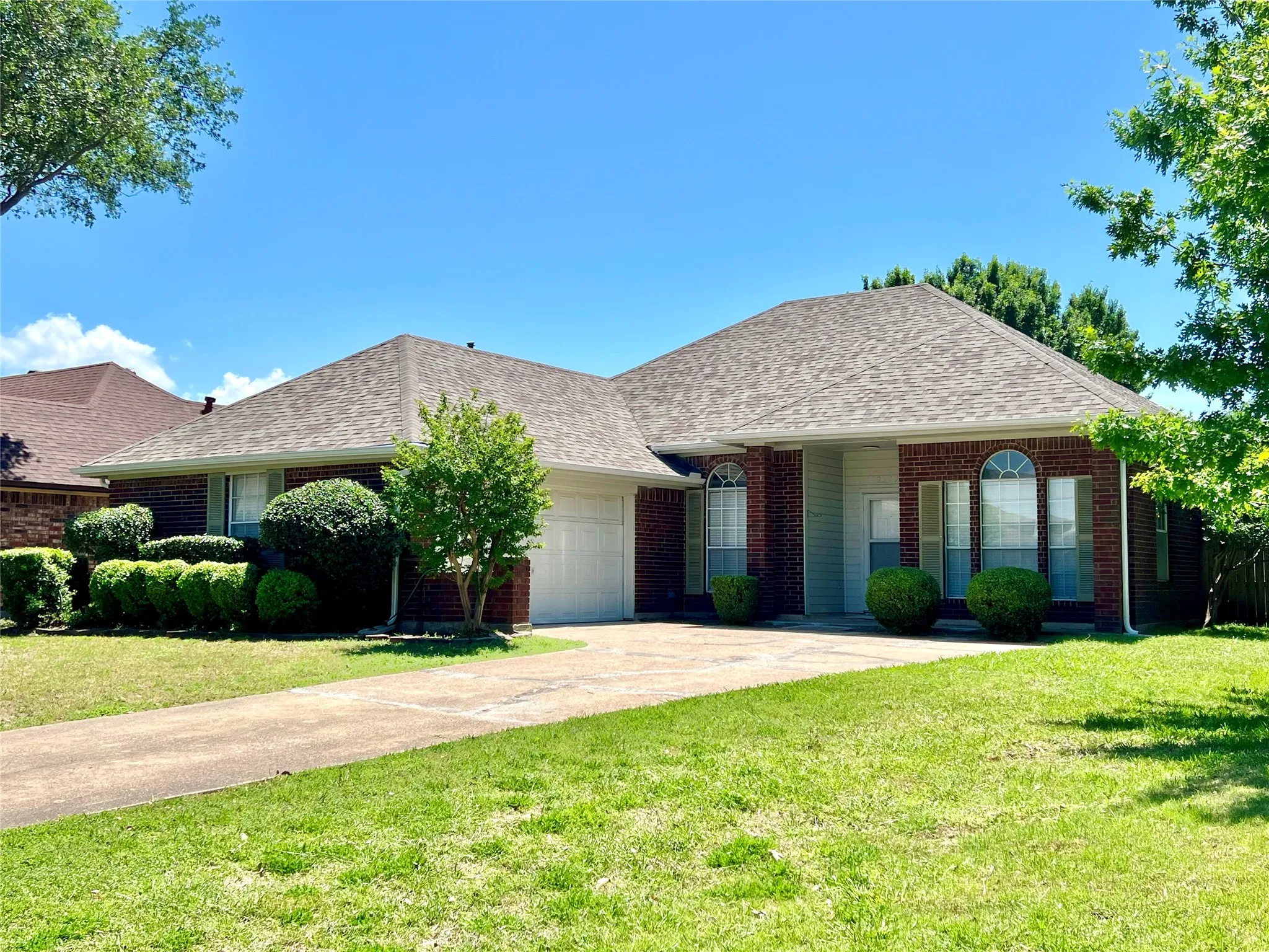 Ranch-style house with roof with shingles, driveway, brick siding, an attached garage, and a front yard