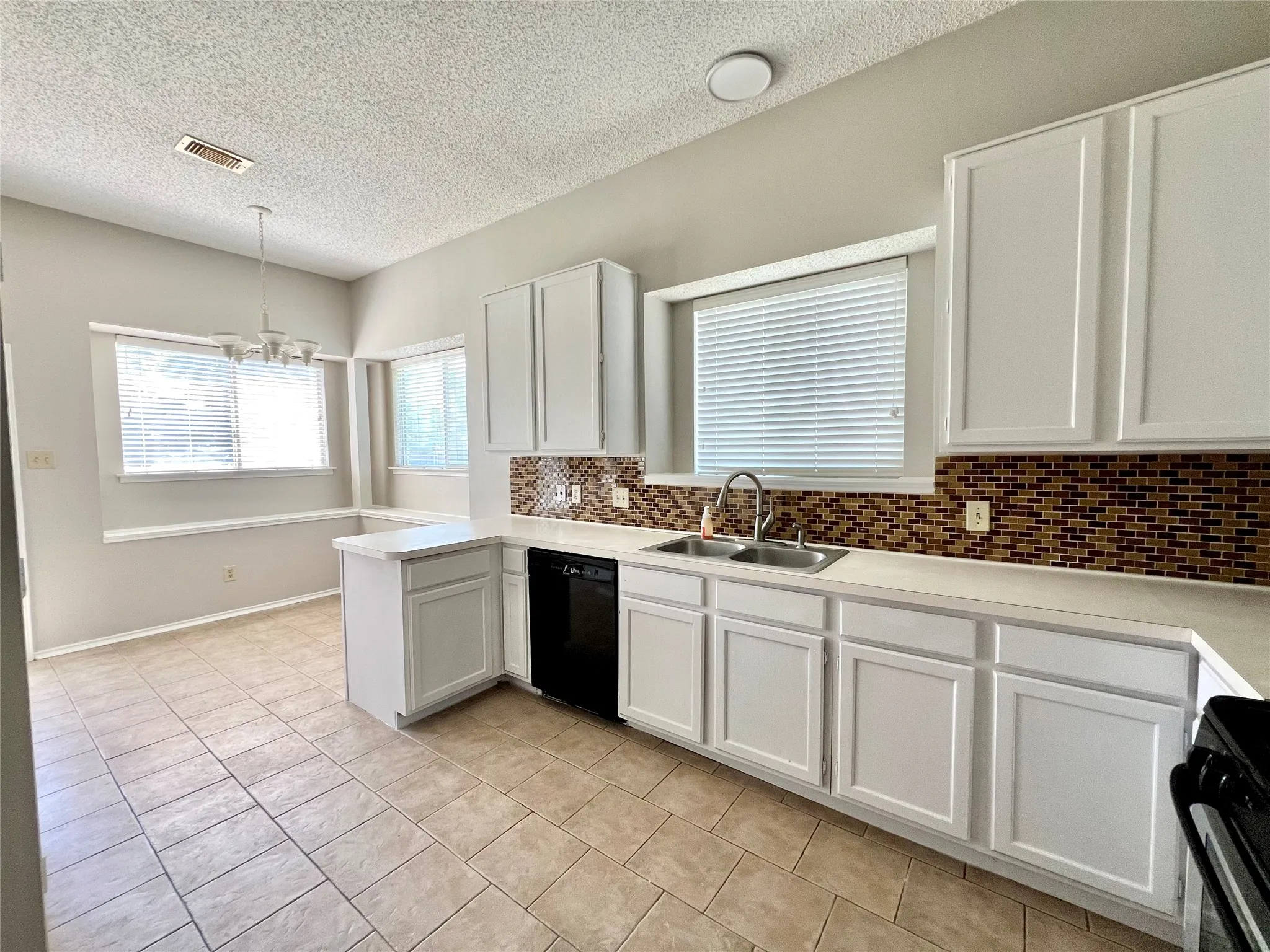 Kitchen featuring dishwasher, visible vents, a sink, a textured ceiling, and range