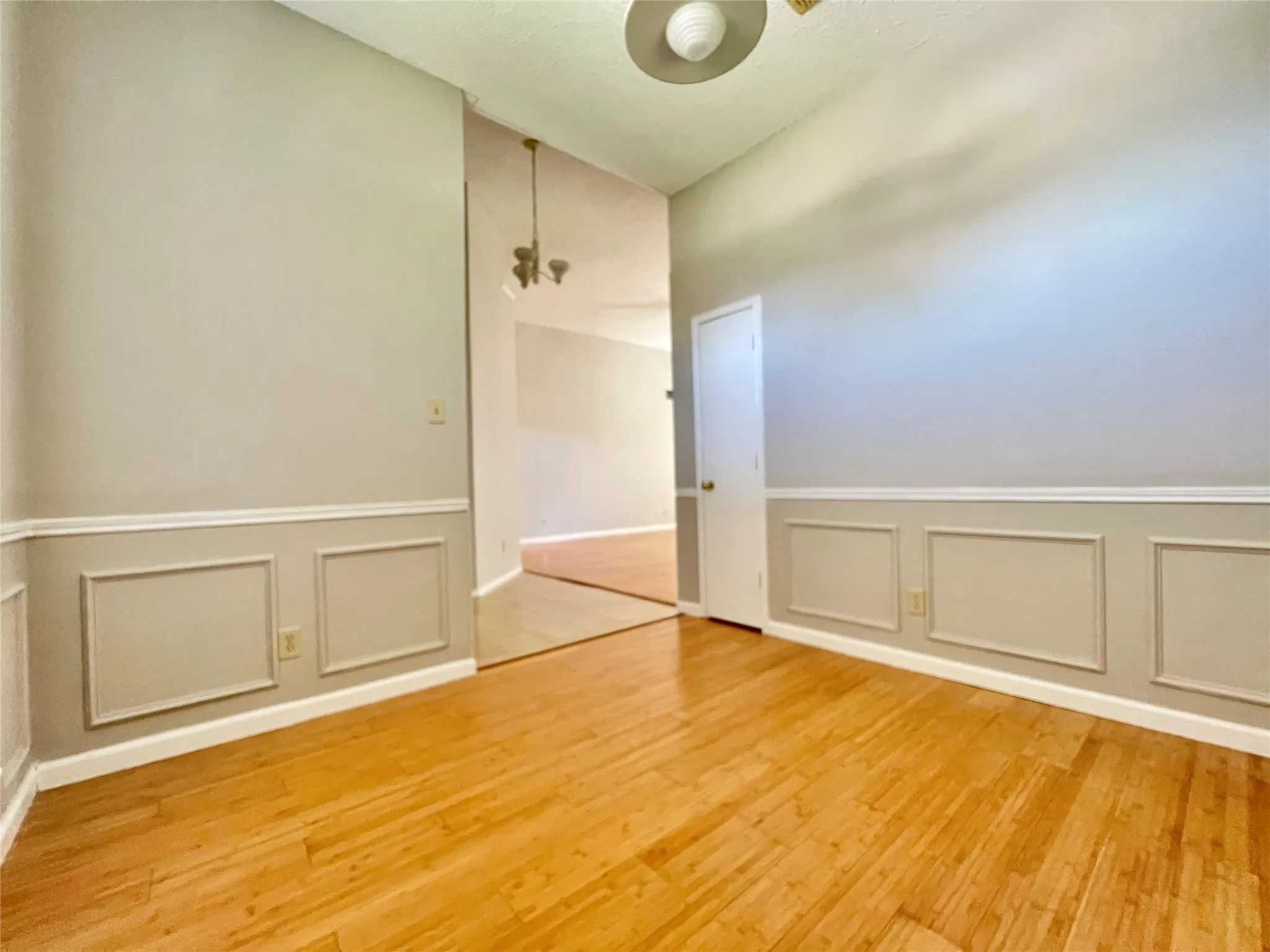 Empty room featuring light wood finished floors, a wainscoted wall, and a decorative wall