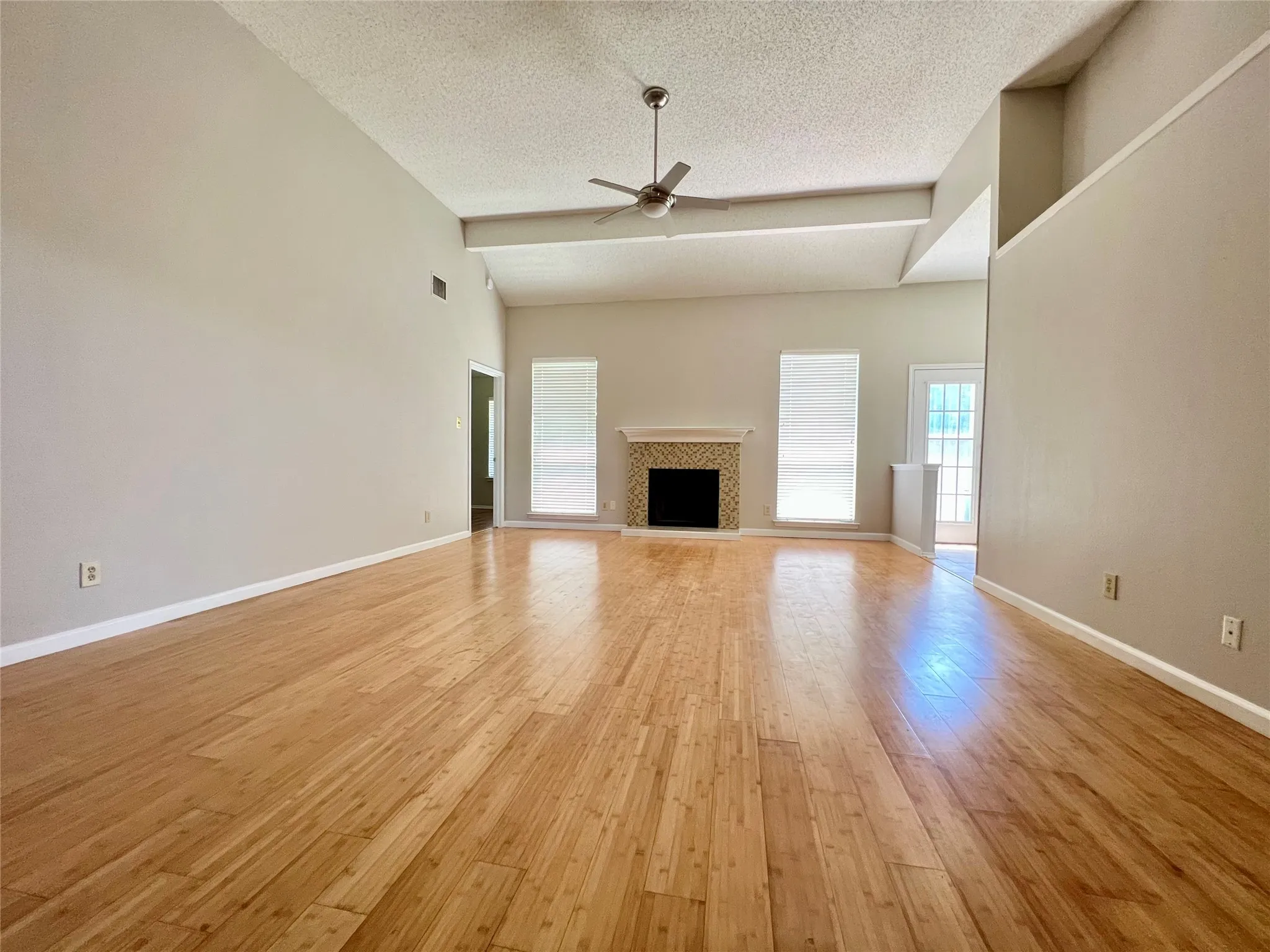 Unfurnished living room with ceiling fan, baseboards, a textured ceiling, and light wood-type flooring
