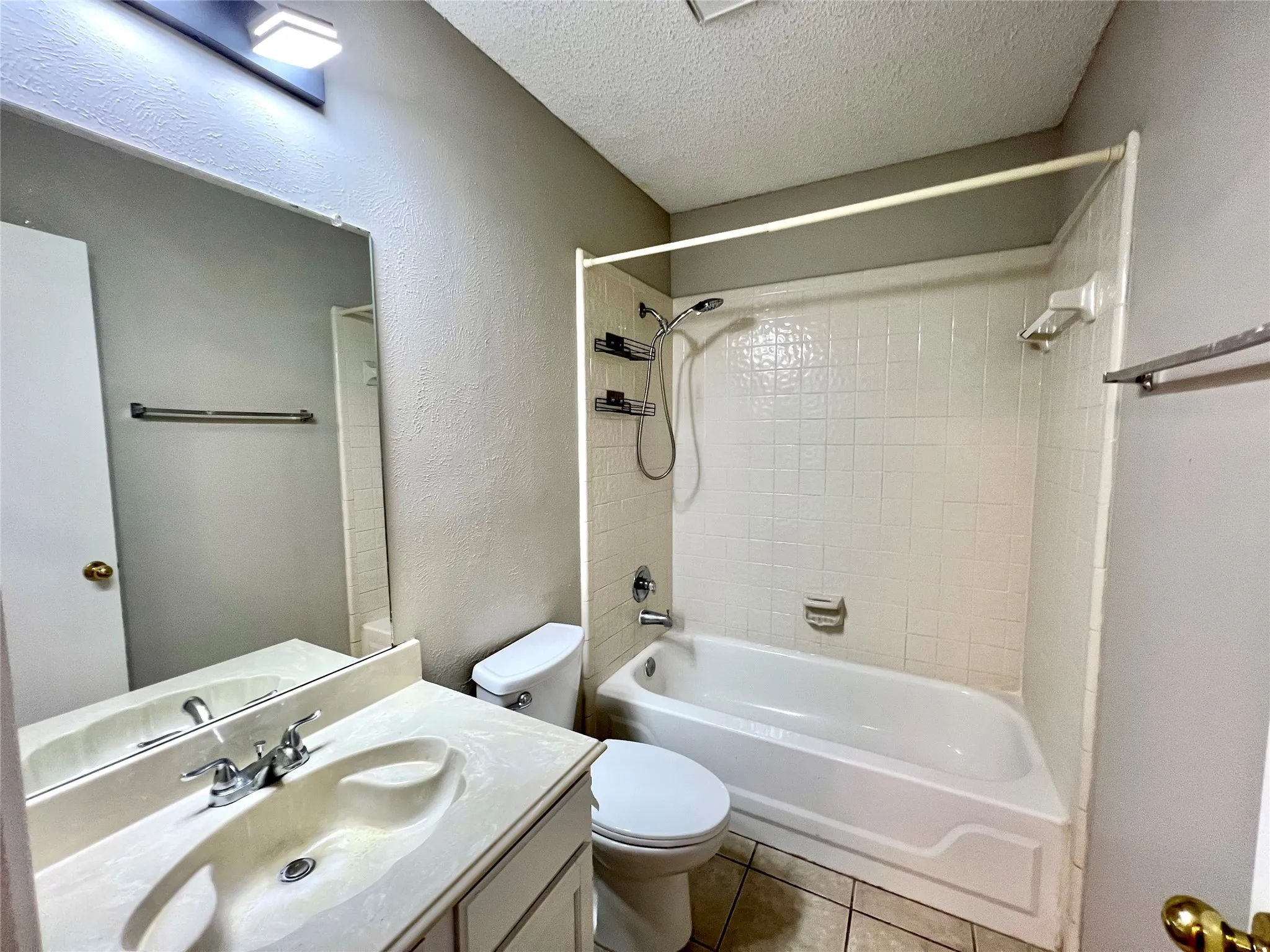 Bathroom with tile patterned floors, shower / bathtub combination, toilet, vanity, and a textured ceiling