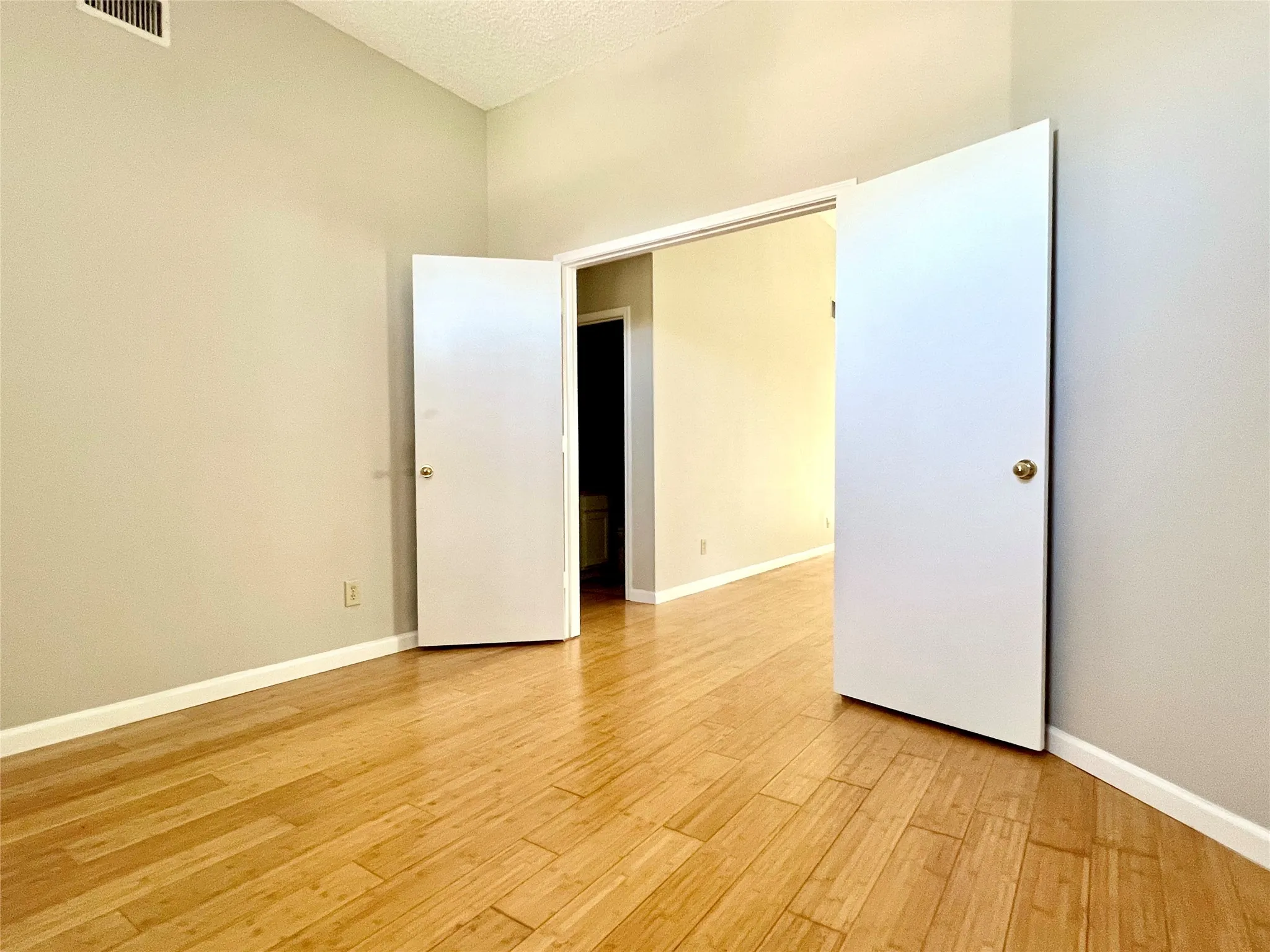 Empty room featuring a textured ceiling, visible vents, light wood finished floors, and baseboards