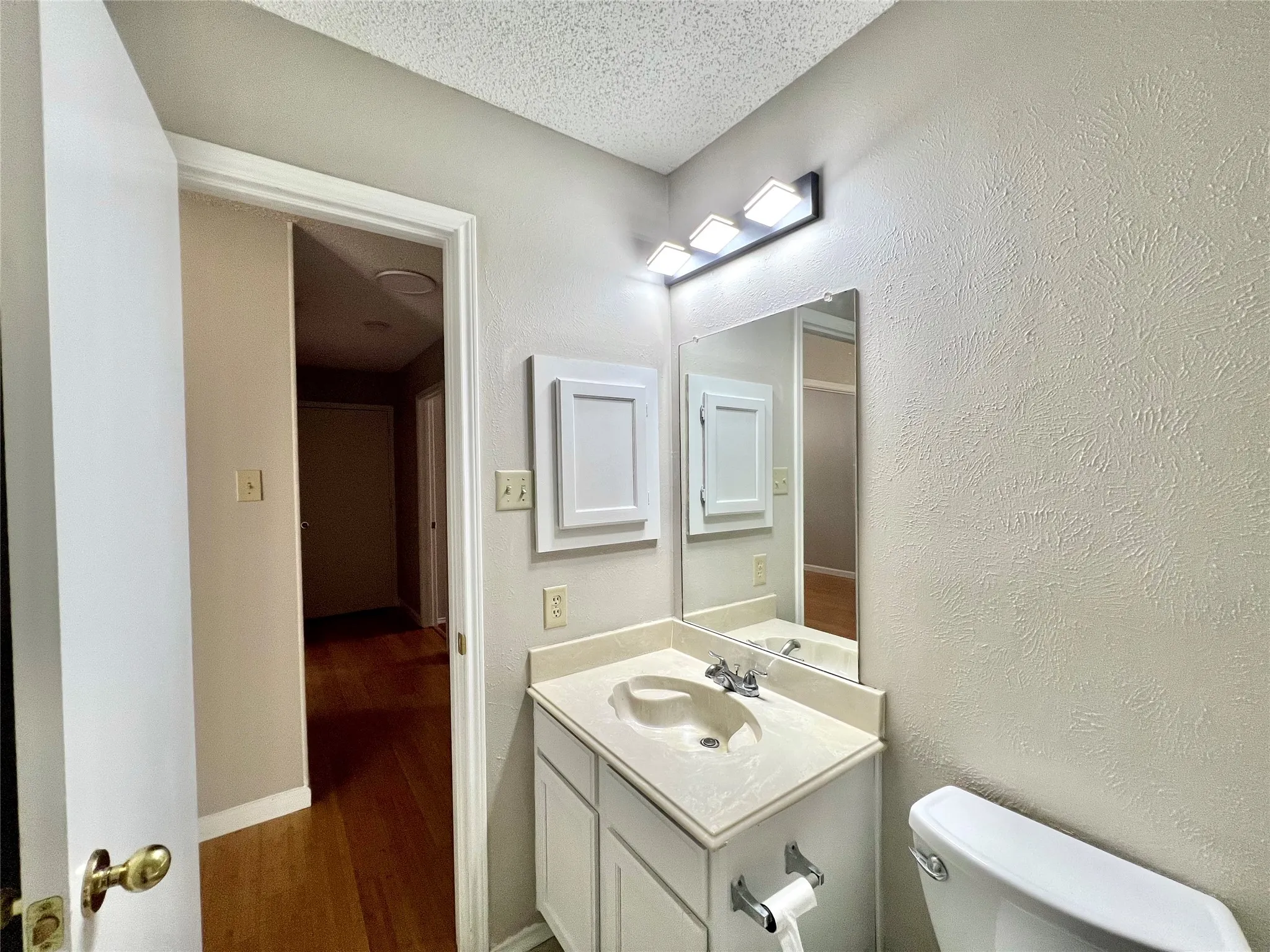 Half bathroom featuring toilet, vanity, wood finished floors, and a textured ceiling