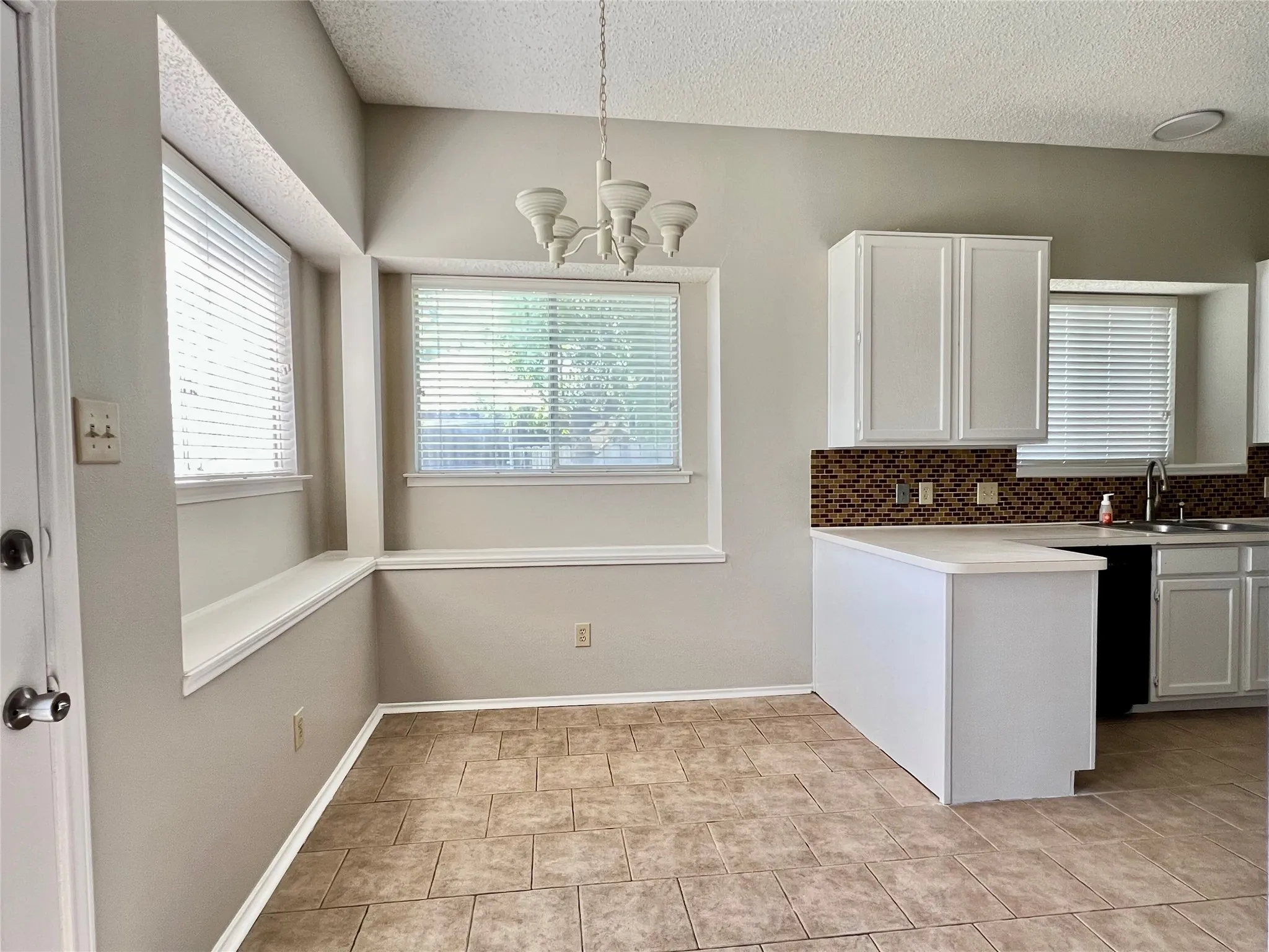 Kitchen with a sink, an inviting chandelier, a textured ceiling, and tasteful backsplash