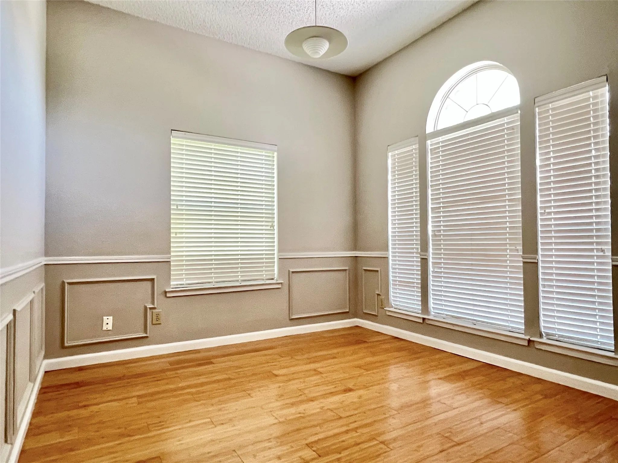 Unfurnished room with light wood-type flooring, wainscoting, and a textured ceiling