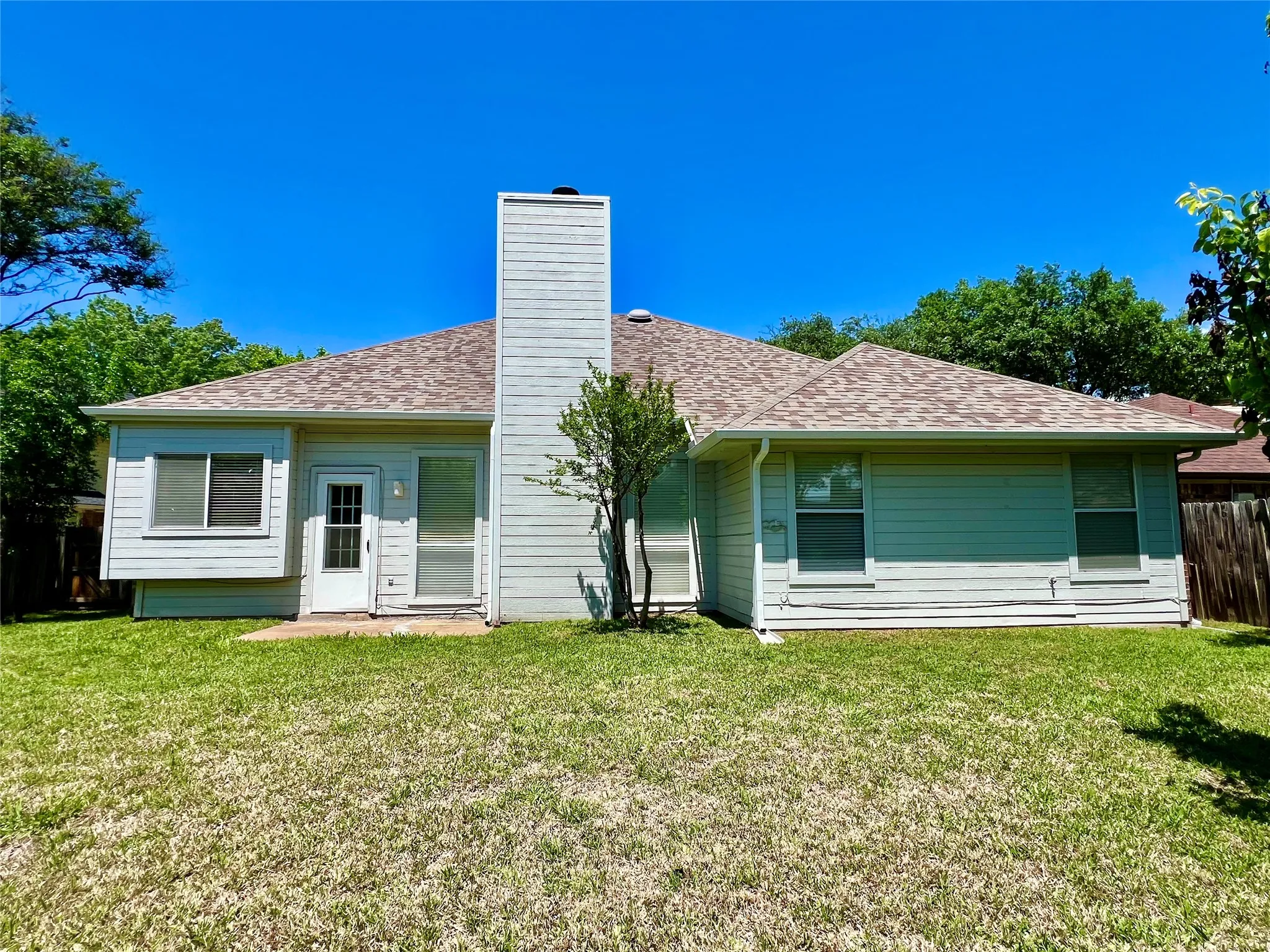 Back of house with fence, a lawn, a shingled roof, and a chimney
