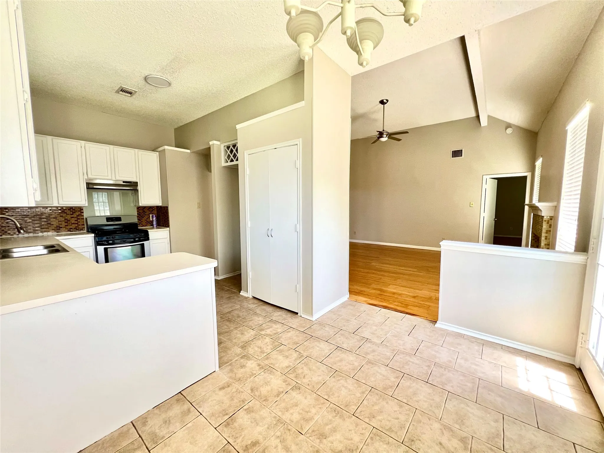 Kitchen featuring stainless steel gas stove, light tile patterned floors, a sink, decorative backsplash, and ceiling fan