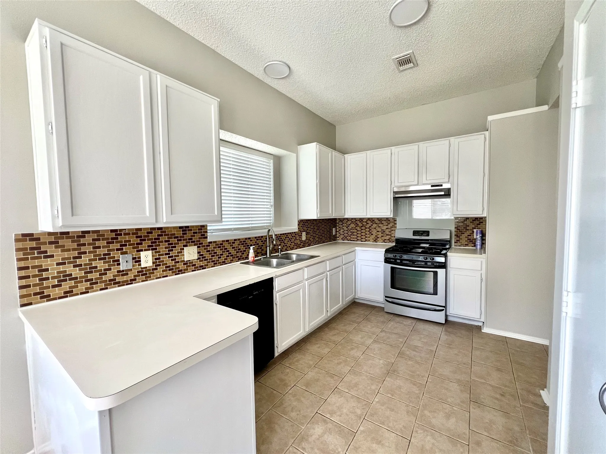 Kitchen featuring stainless steel range with gas cooktop, a sink, decorative backsplash, dishwasher, and visible vents