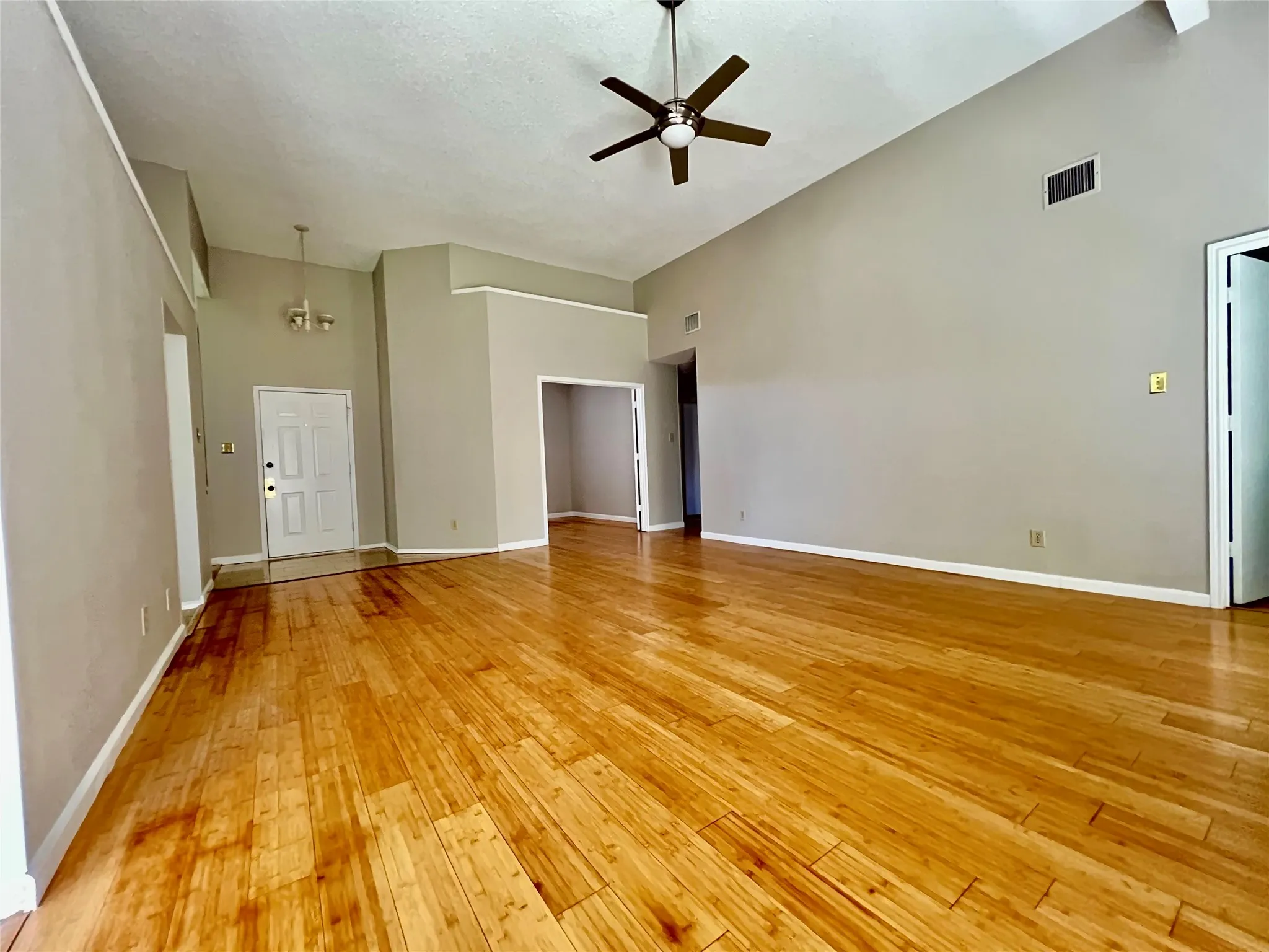 Unfurnished living room with light wood-type flooring, a ceiling fan, visible vents, and high vaulted ceiling