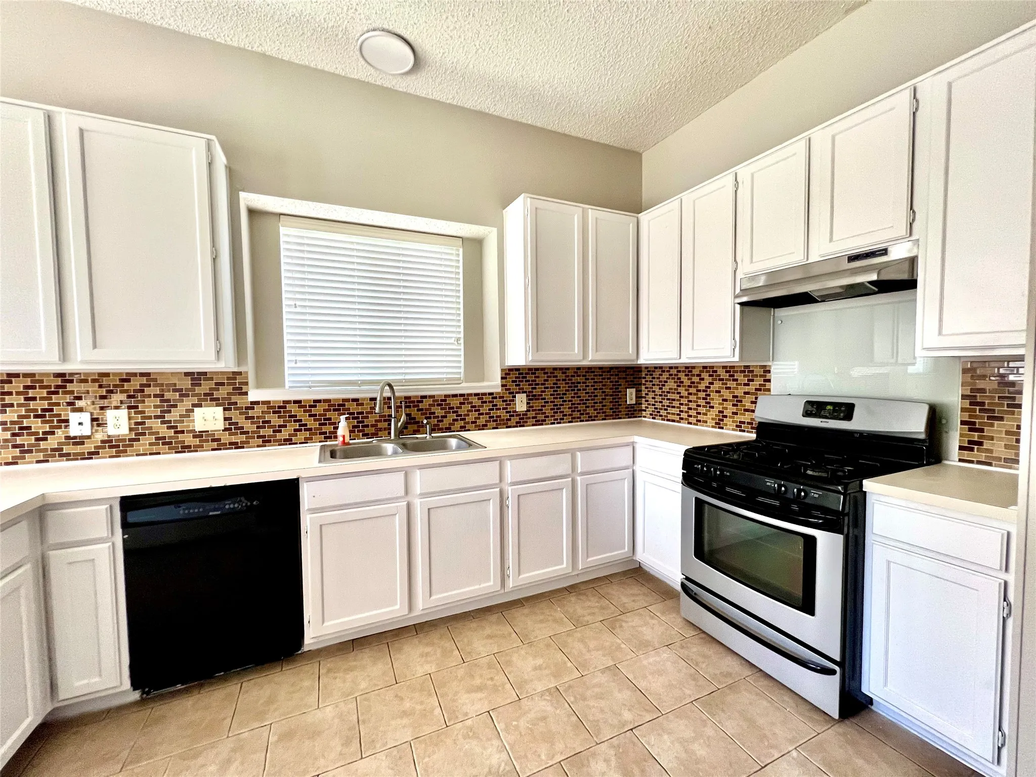 Kitchen featuring a sink, stainless steel gas stove, white cabinets, under cabinet range hood, and black dishwasher
