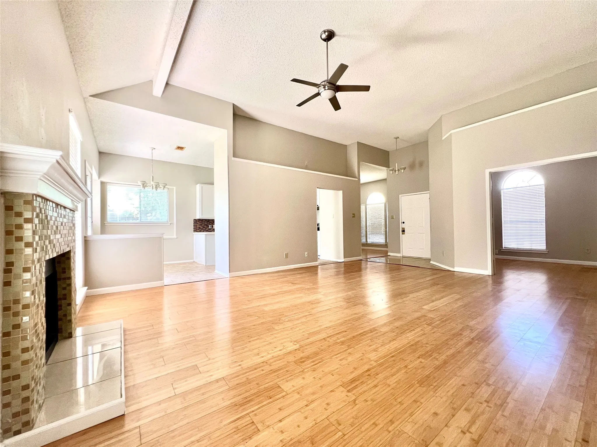 Unfurnished living room featuring a textured ceiling, beam ceiling, light wood finished floors, and ceiling fan with notable chandelier