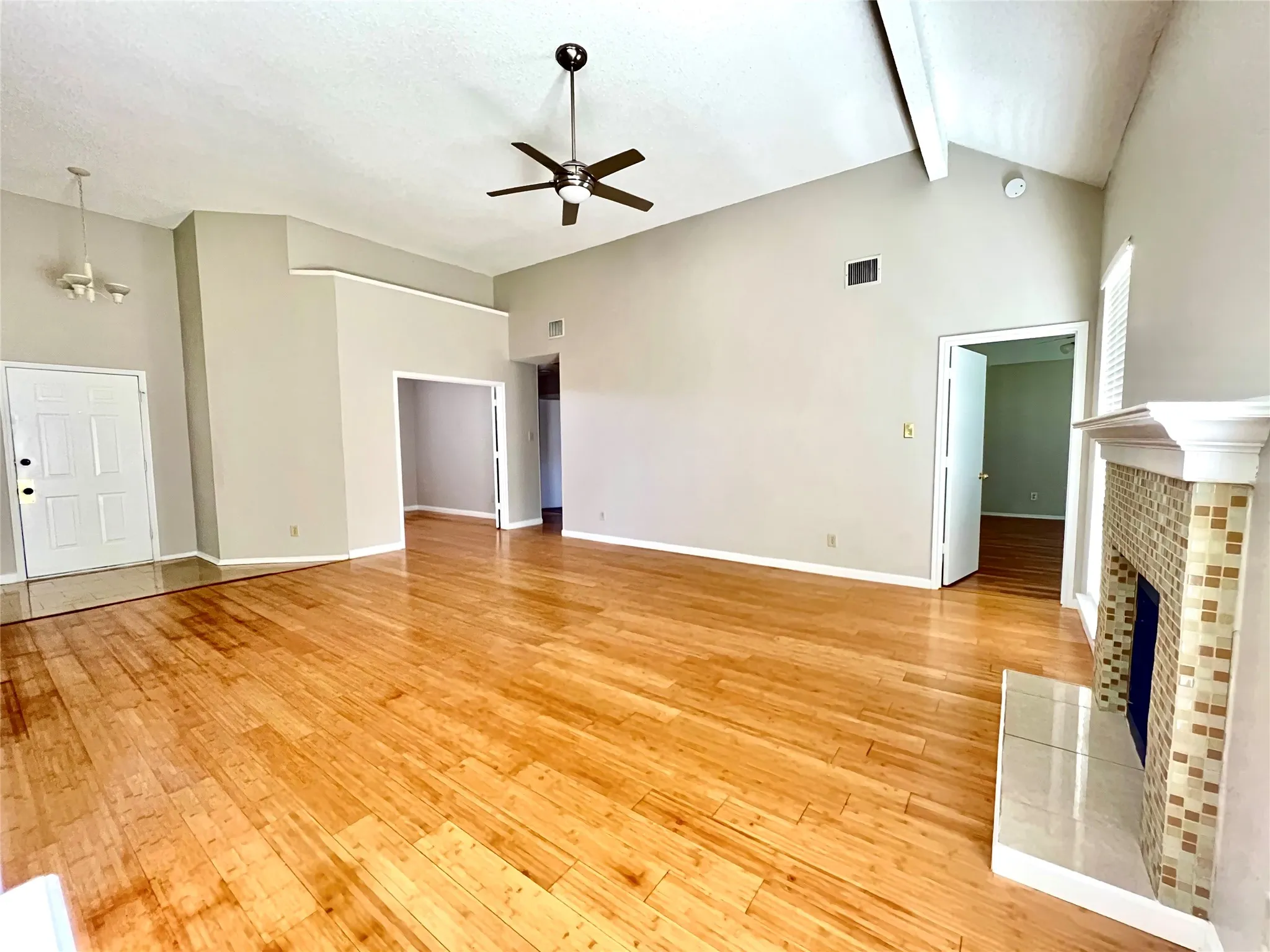 Unfurnished living room featuring visible vents, light wood-style floors, ceiling fan with notable chandelier, a tile fireplace, and high vaulted ceiling