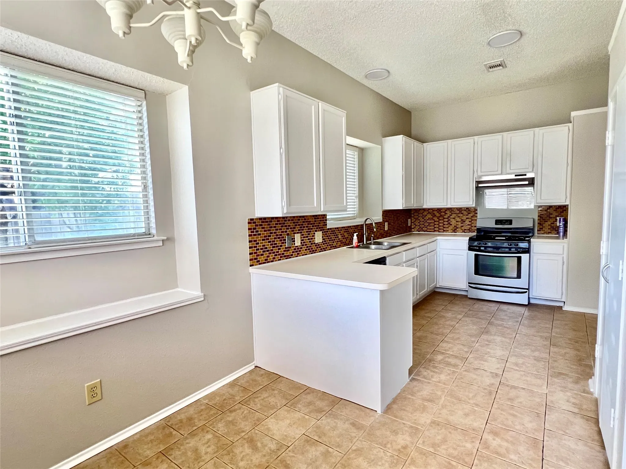 Kitchen featuring white cabinets, stainless steel gas range oven, light tile patterned floors, a sink, and decorative backsplash