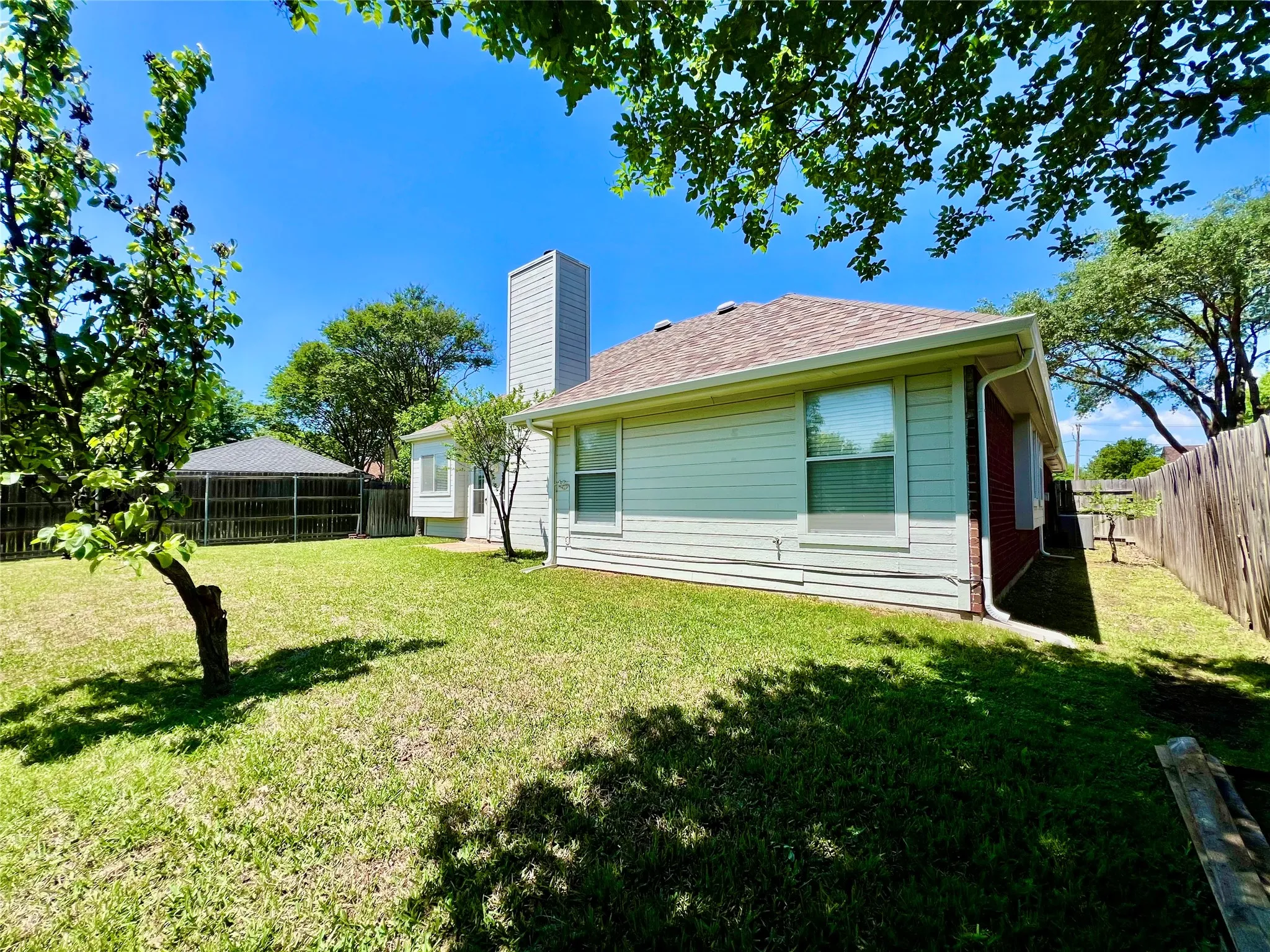 Rear view of house with a fenced backyard, a chimney, brick siding, a shingled roof, and a yard